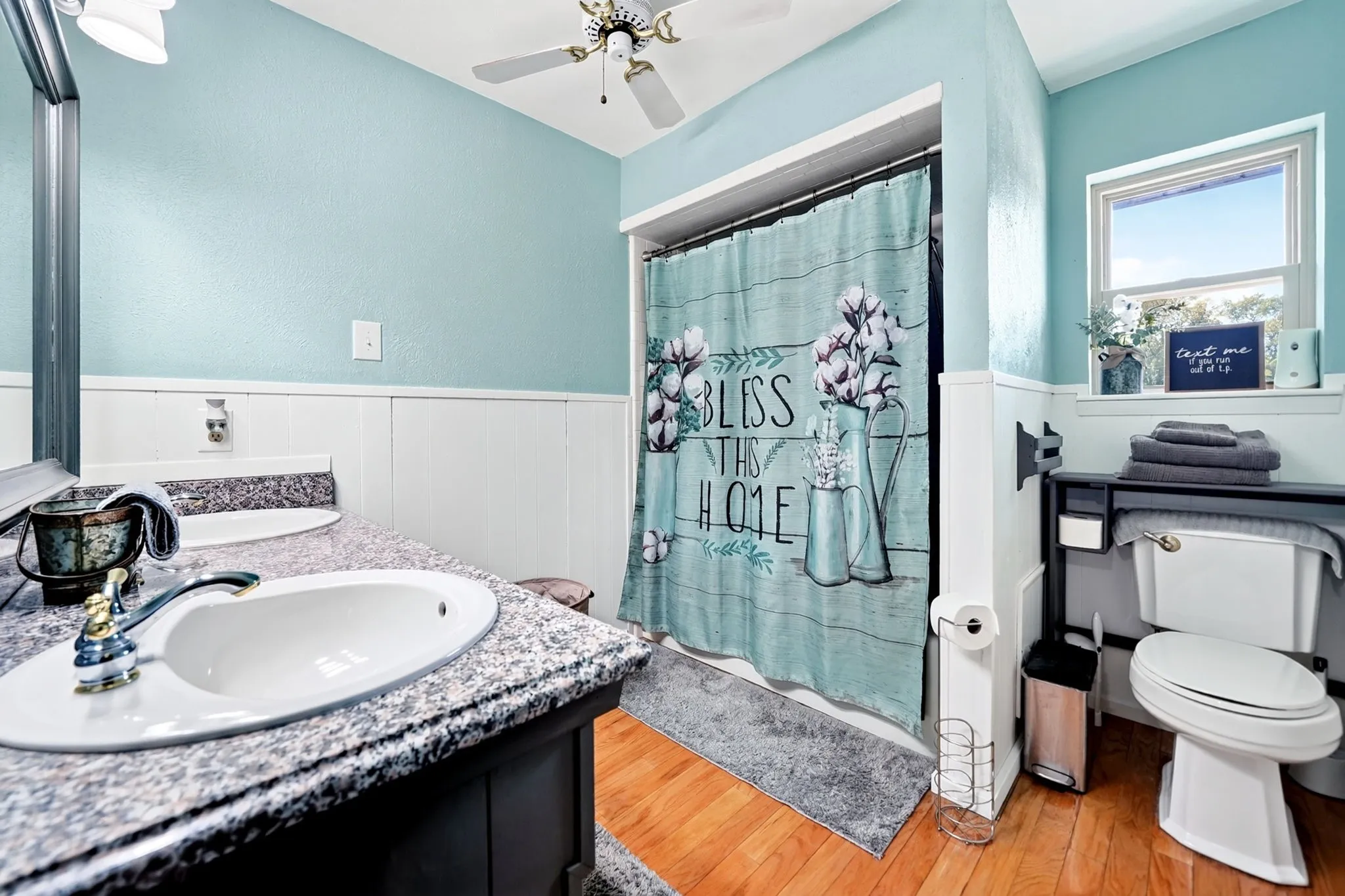 Vanity with a granite-style countertop and undermount sink, wood-finish flooring, a ceiling fan, and a window providing natural light