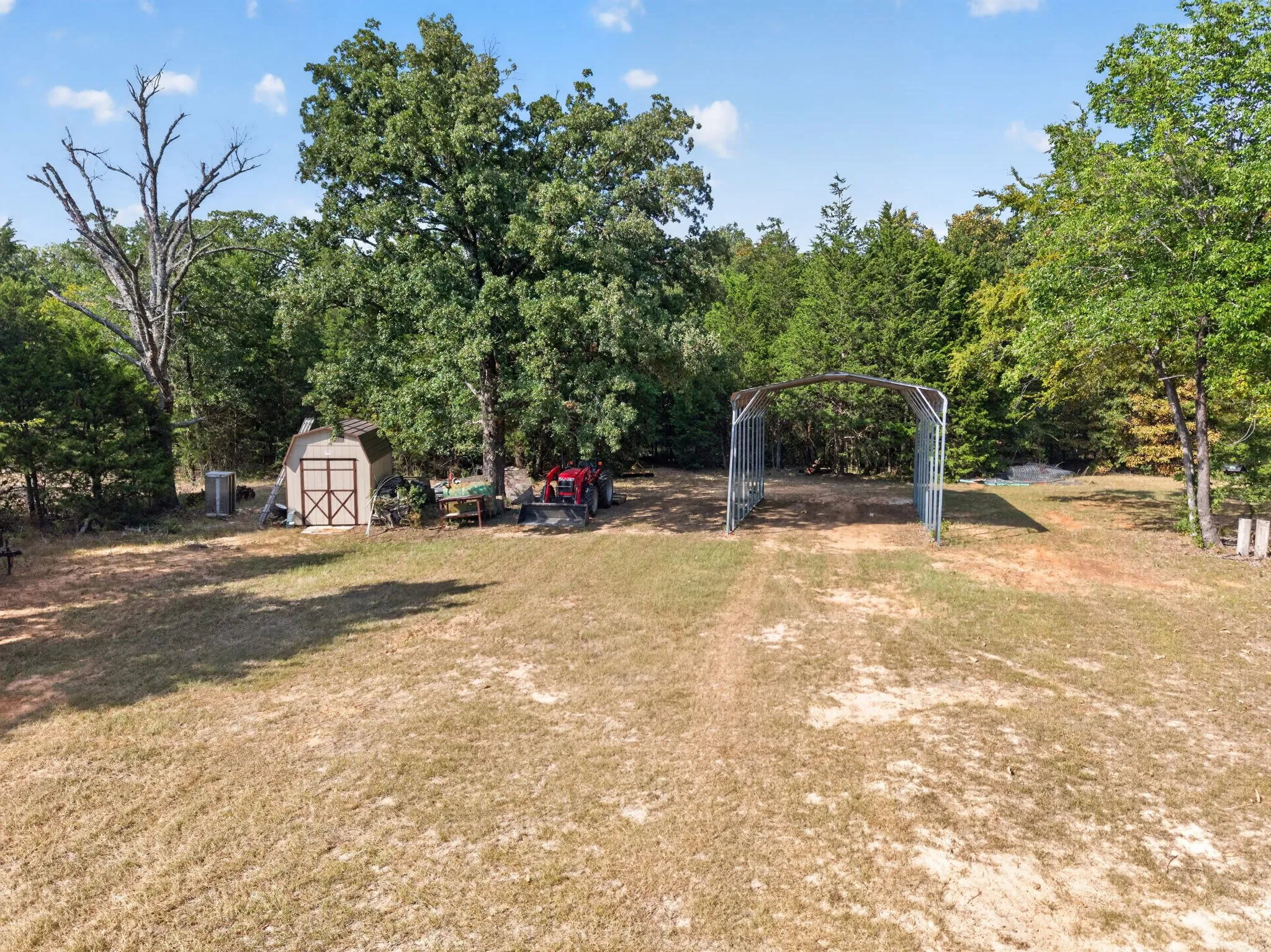 Expansive outdoor space featuring a storage shed, mature trees, and a metal frame structure