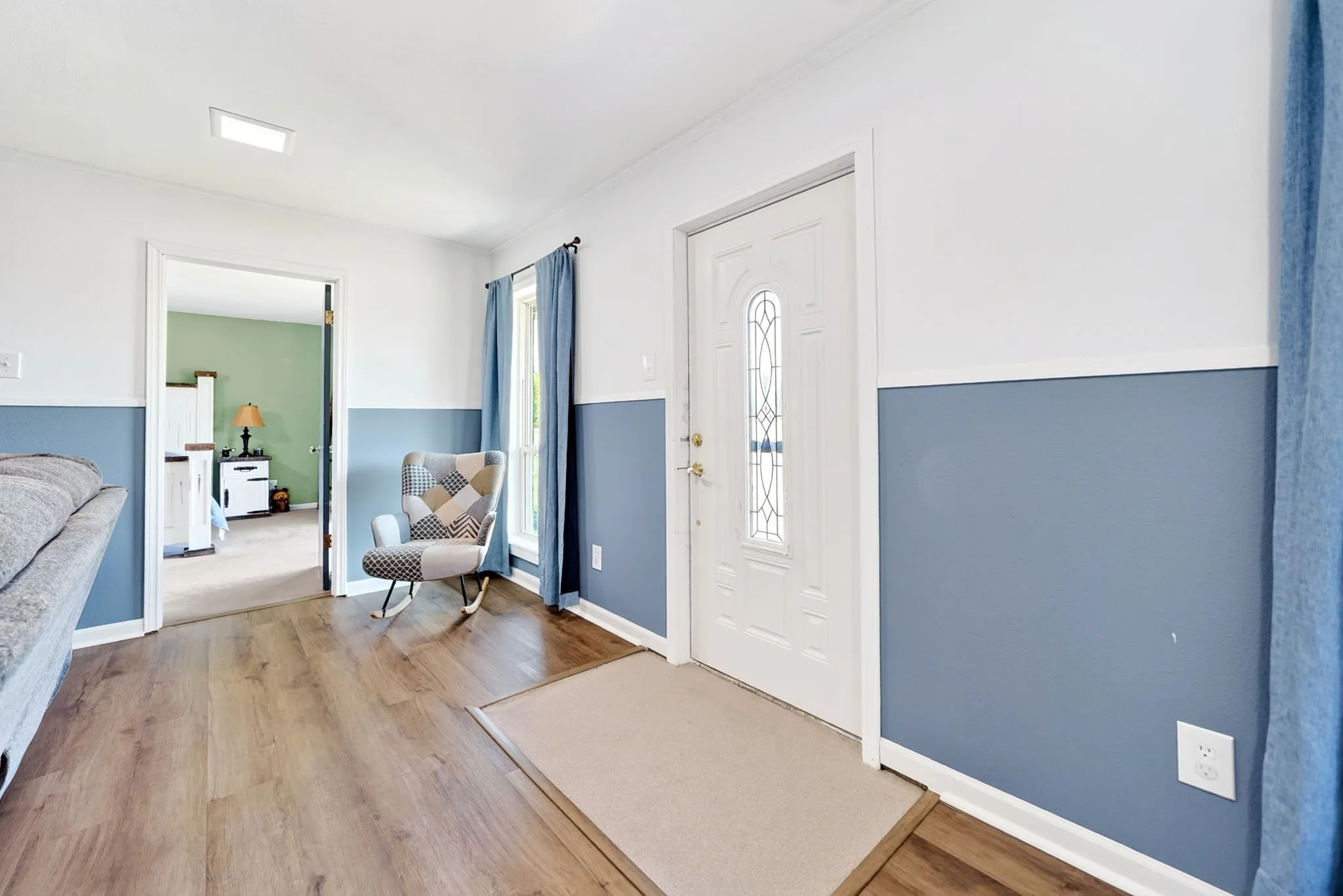 Wood-finish flooring, white paneled entry door with decorative glass, and a rectangular ceiling light fixture