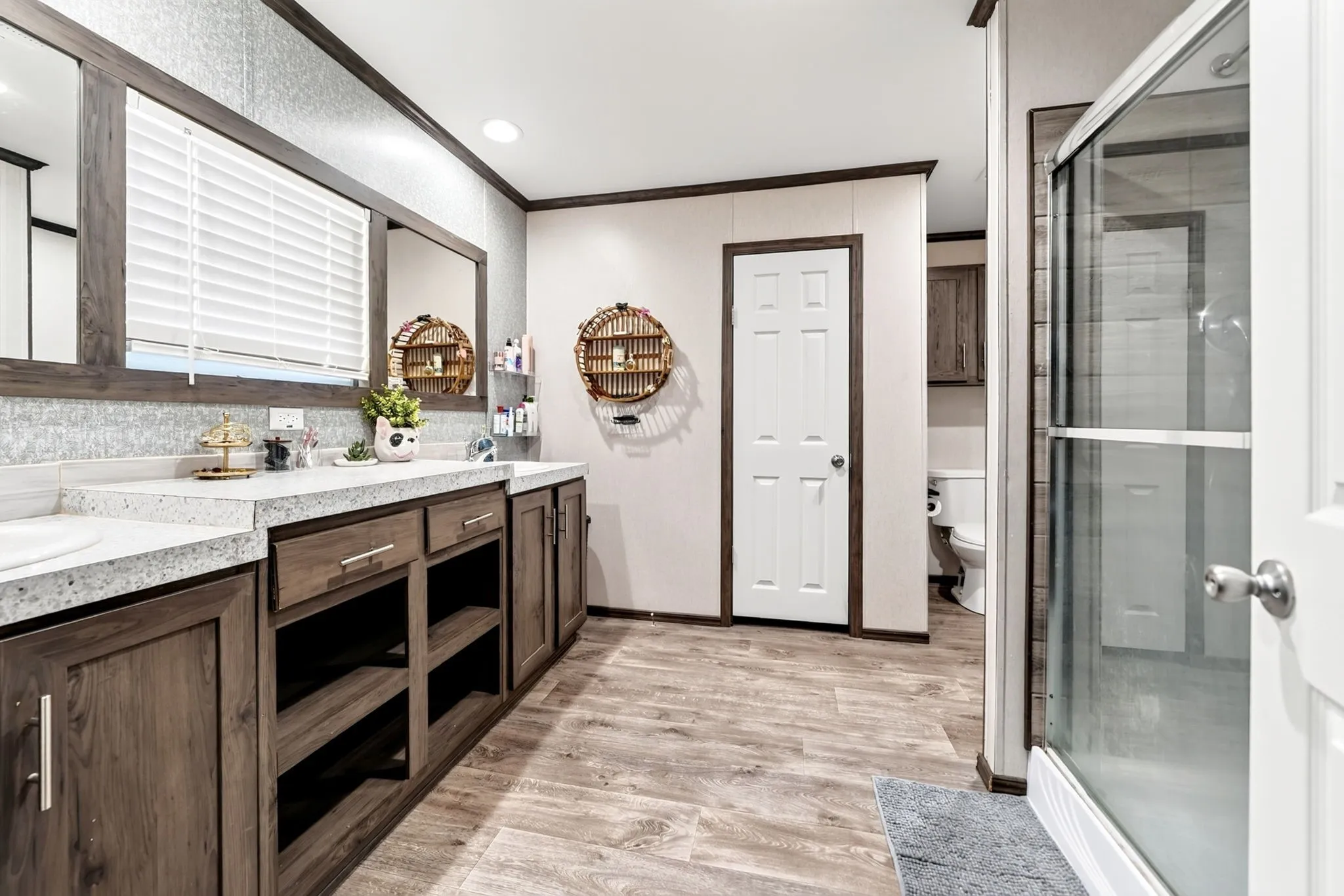 Dual vanity with integrated sinks, wood-finish cabinetry with open shelving, wood-finish flooring, and a glass-enclosed shower