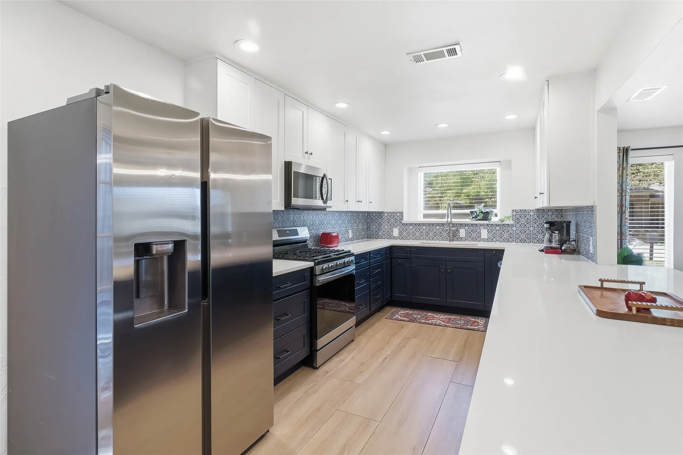 Modern kitchen featuring stainless steel appliances, two-tone cabinetry, wood-finish flooring, recessed lighting, and a white countertop