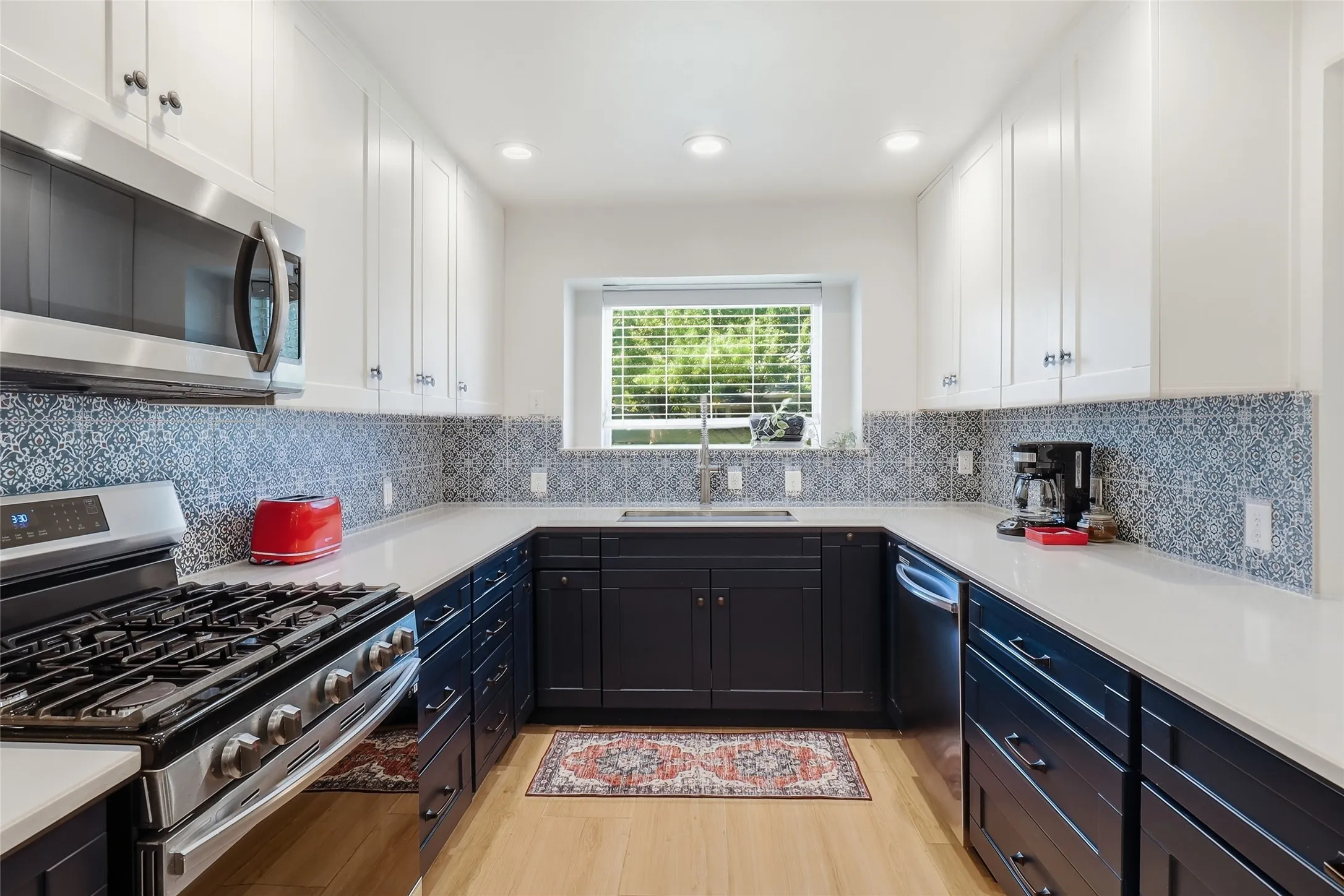 Modern kitchen with two-tone cabinetry, stainless steel appliances, quartz countertops, and a patterned tile backsplash