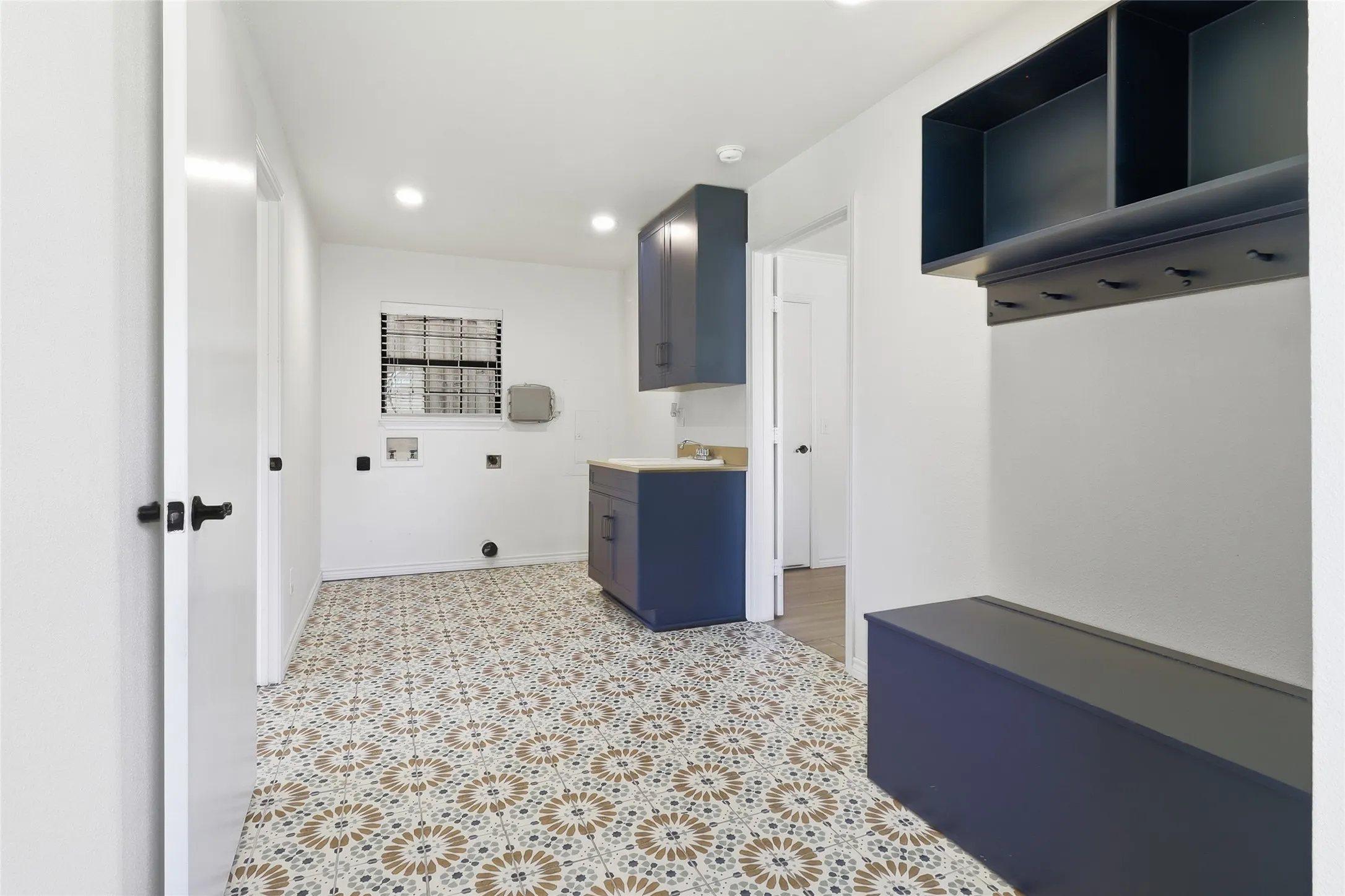 Laundry room featuring patterned tile flooring, built-in cabinetry, a utility sink, and a window with blinds