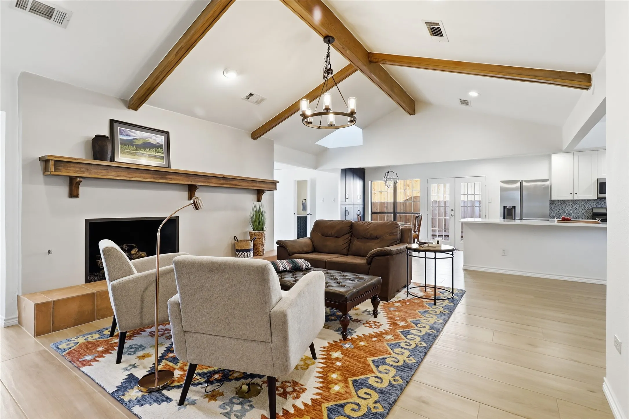 Vaulted ceiling with exposed wood beams, wood-finish flooring, built-in fireplace, double French doors.