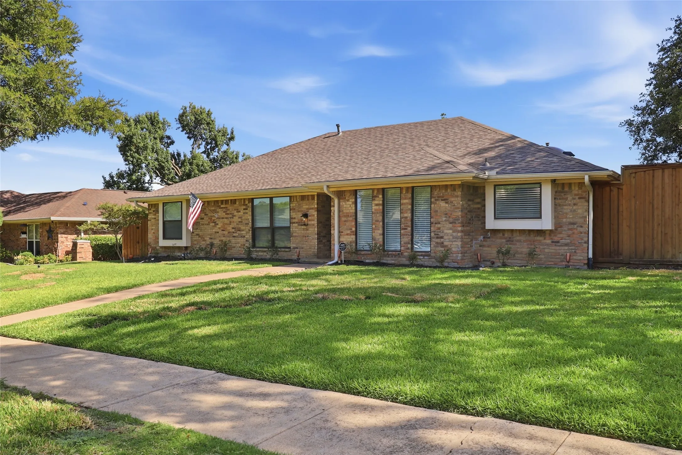 Brick exterior, pitched shingle roof, established front lawn, concrete walkway, and privacy fencing