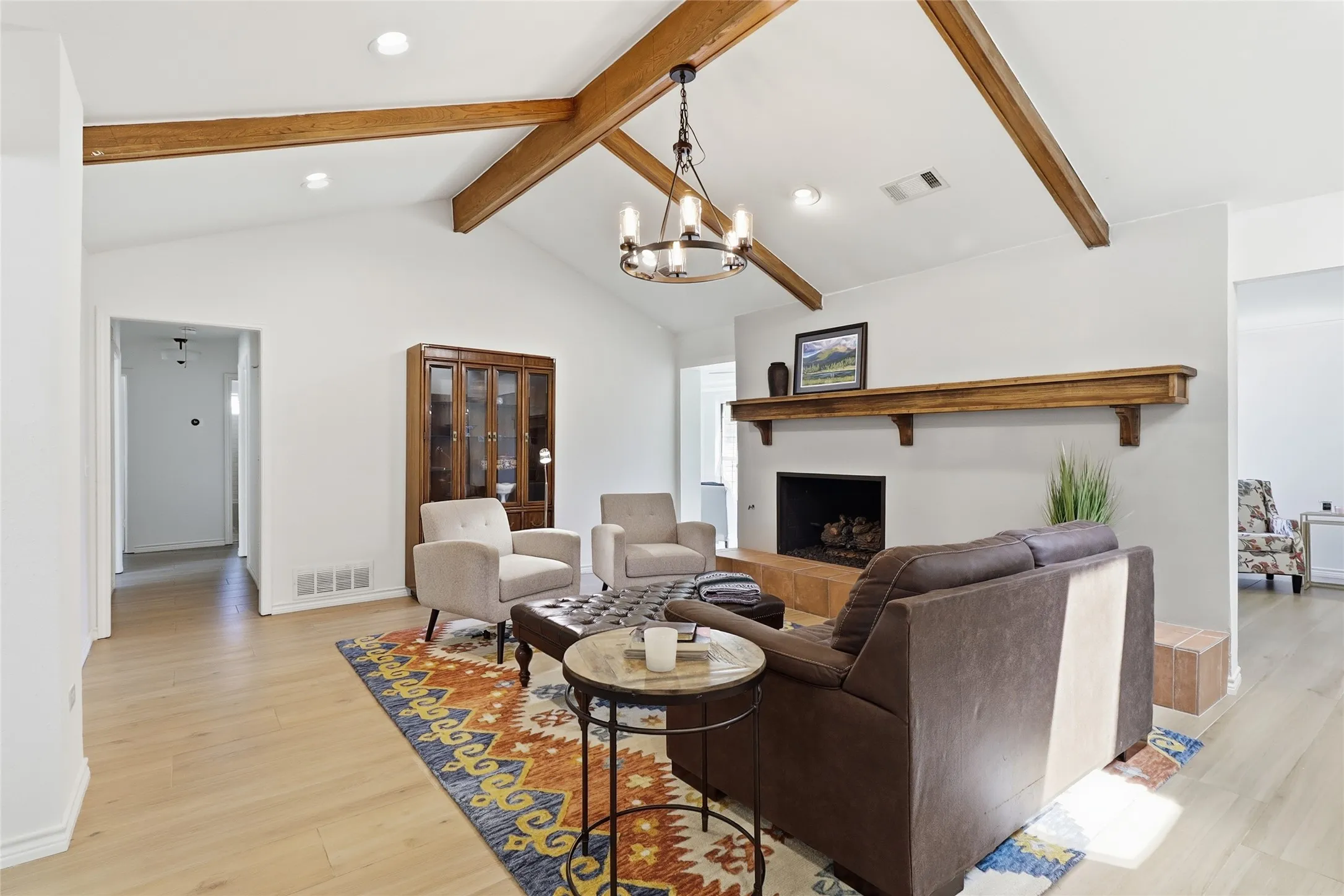 Vaulted ceiling with exposed wood beams, wood-finish flooring, fireplace with a wood mantle, and an iron chandelier
