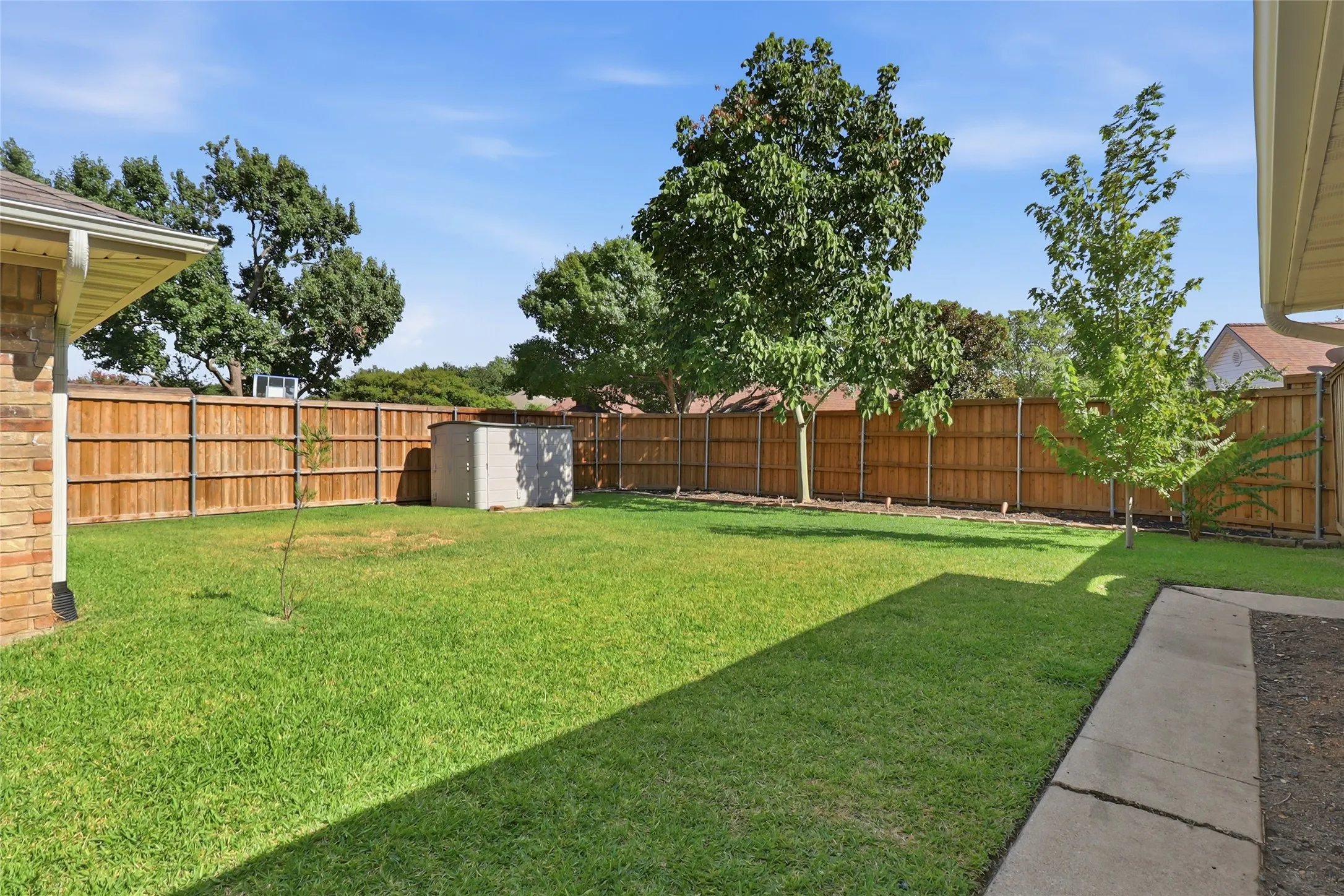 Expansive grassy yard with mature trees, a privacy fence, and a storage shed
