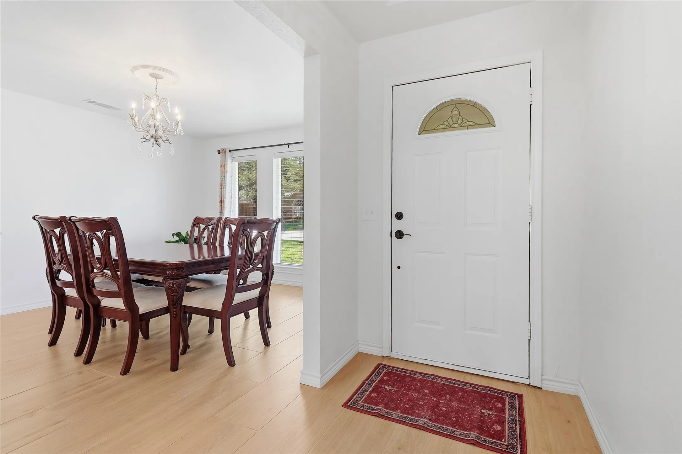 Hardwood-finish flooring, white entry door with decorative glass, and a dining area featuring a chandelier
