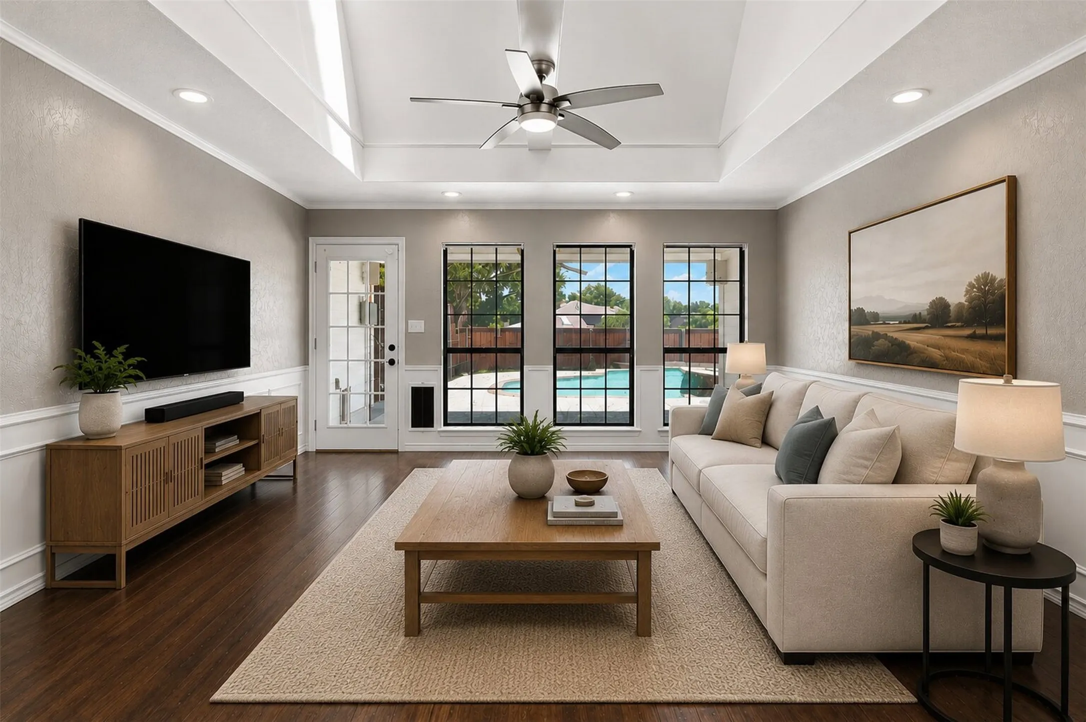Tray ceiling with recessed lighting and a ceiling fan, wood-finish flooring, wainscoting, and multiple windows with a pool beyond