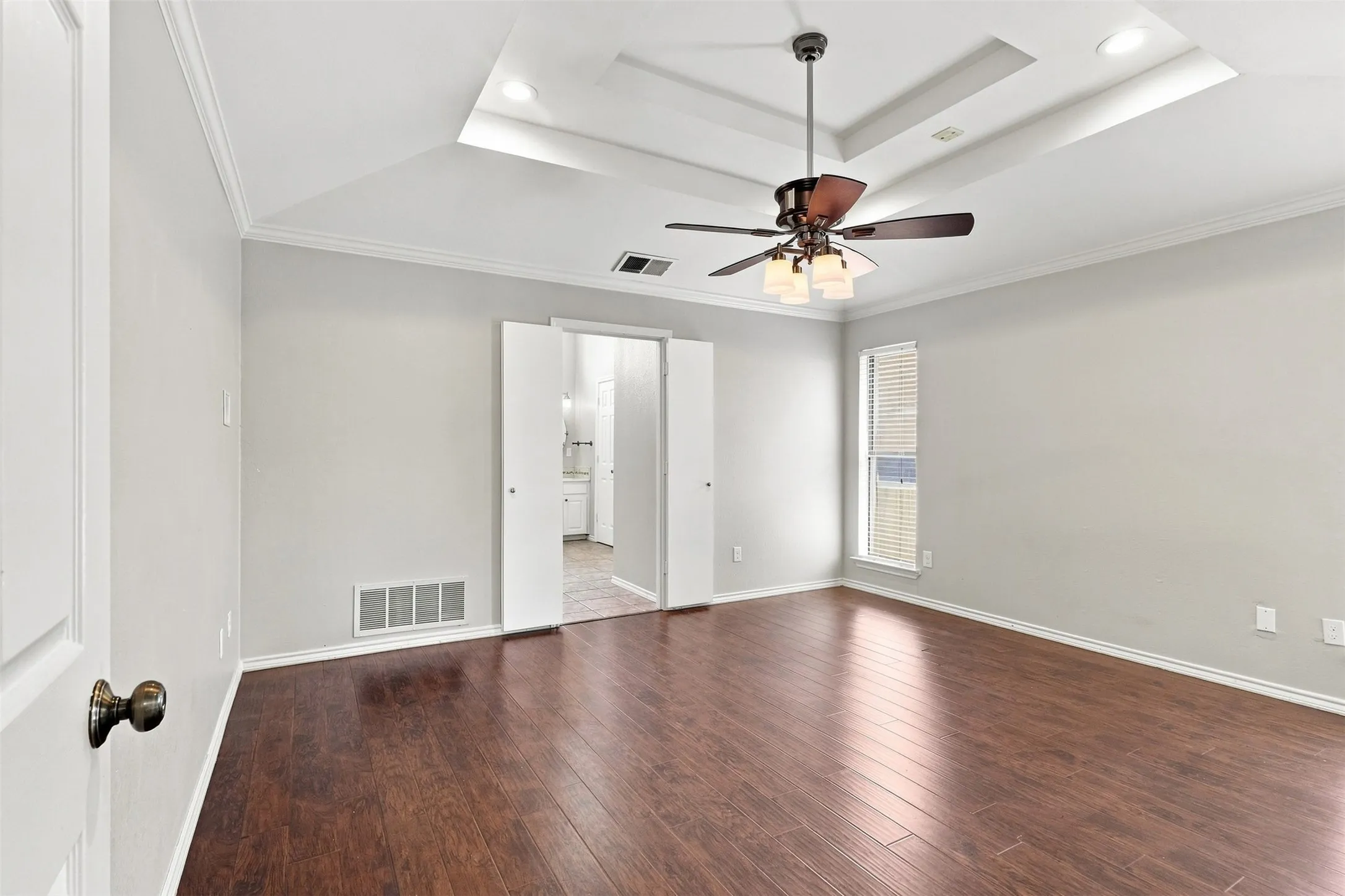 Tray ceiling with a ceiling fan, crown molding, and dark wood-finish flooring