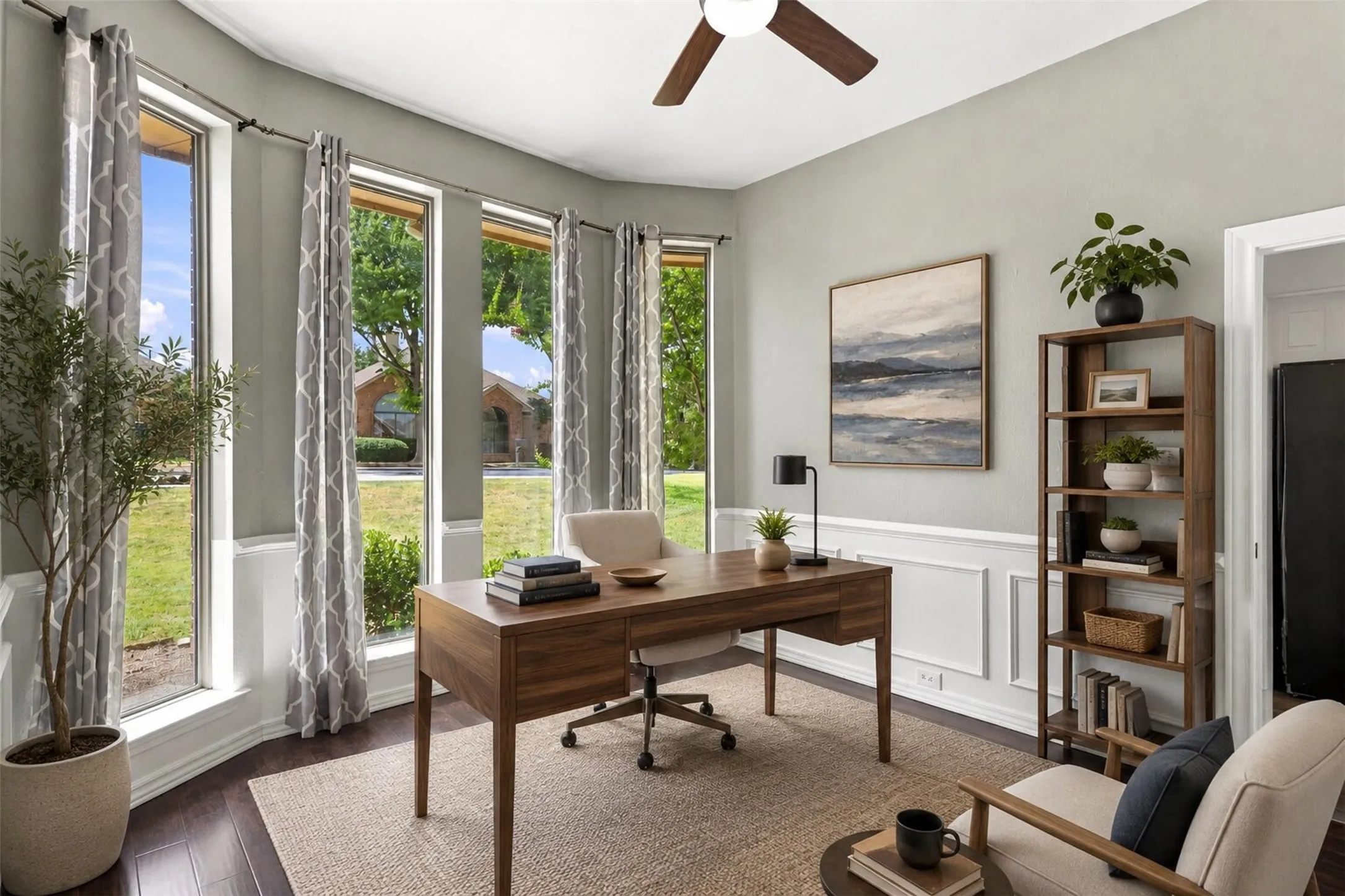 Expansive windows with exterior views, dark wood-finish flooring, ceiling fan, decorative wall paneling, and built-in shelving