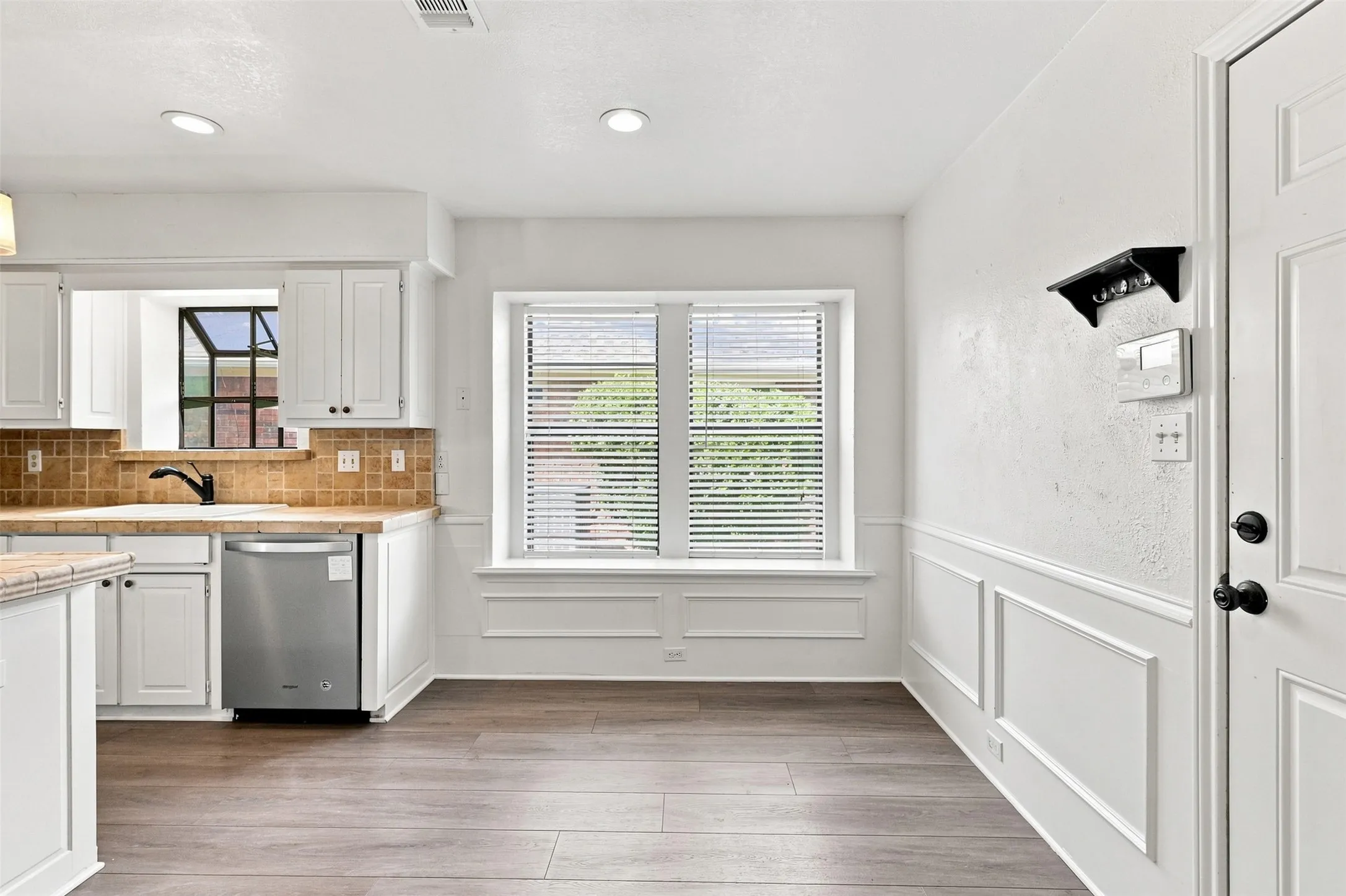Kitchen area with white cabinetry, stainless steel dishwasher, tile backsplash, and recessed lighting