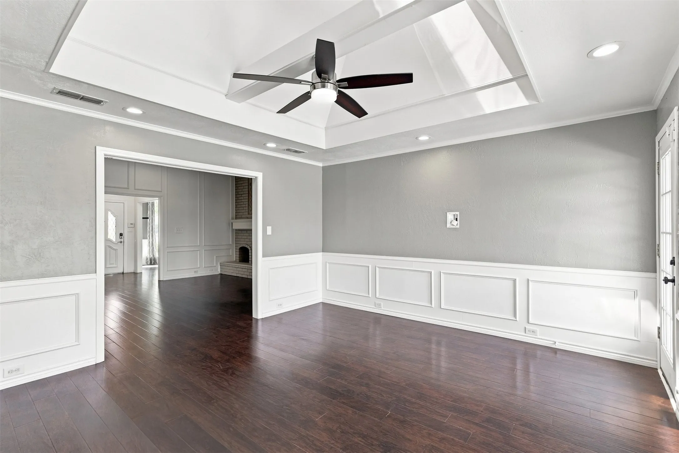 Tray ceiling with recessed lighting, dark wood-finish flooring, white wainscoting, and a ceiling fan