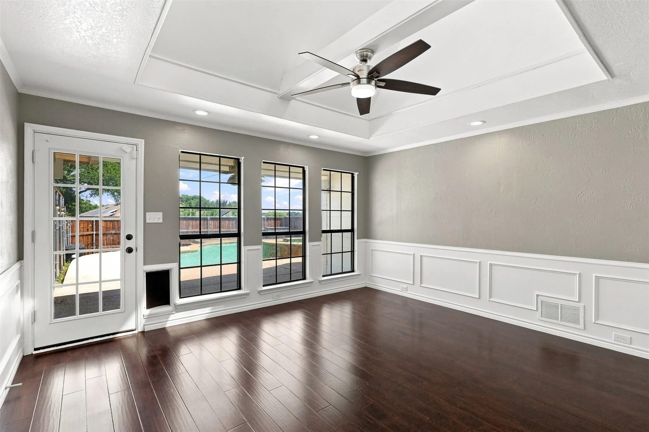 Dark wood-finish flooring, white paneled walls, exposed ceiling beams, recessed lighting, and a white brick fireplace with a decorative mantel