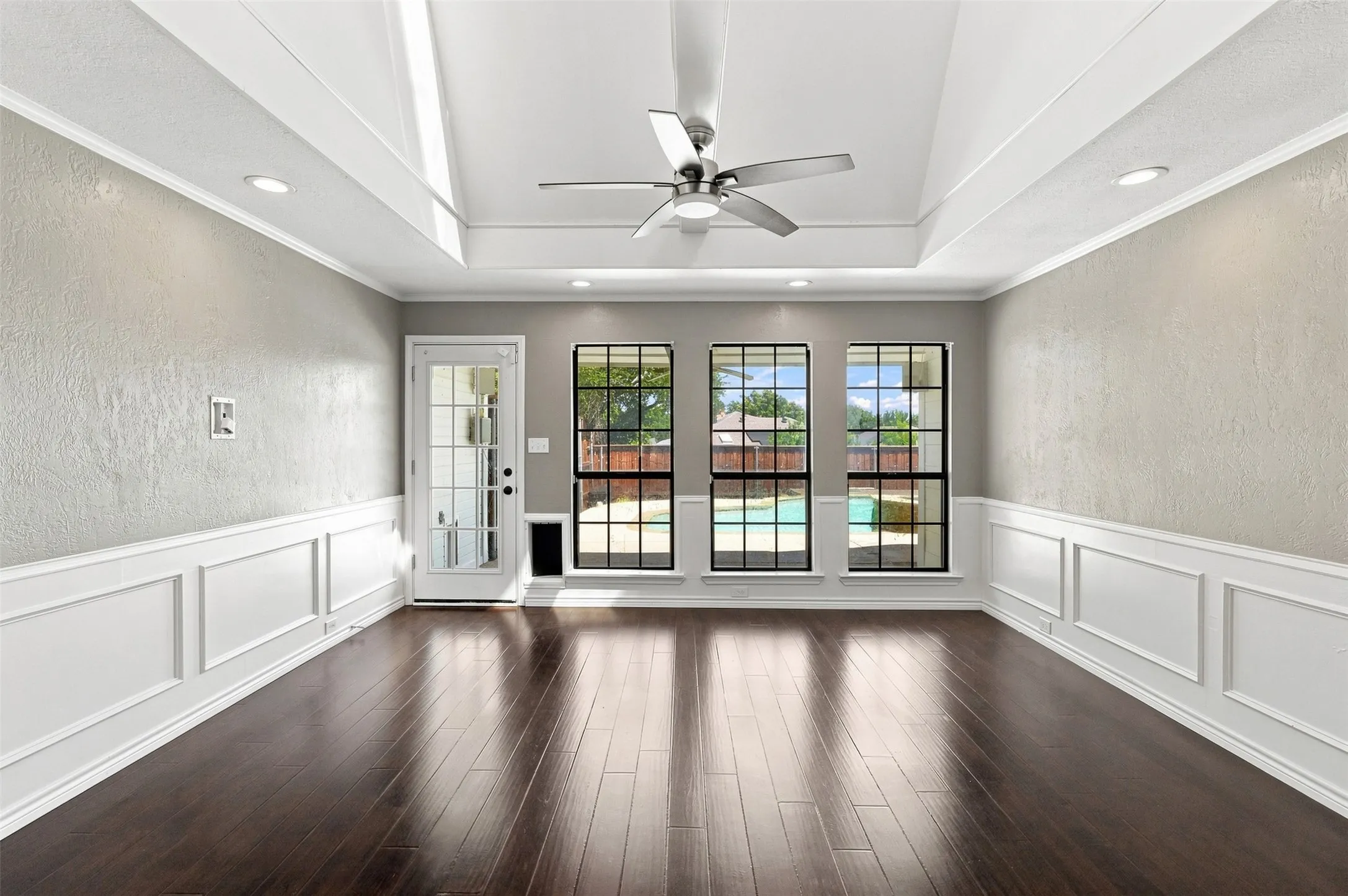 Dark wood-finish flooring, white paneled walls, exposed ceiling beams, recessed lighting, and a white brick fireplace with a decorative mantel