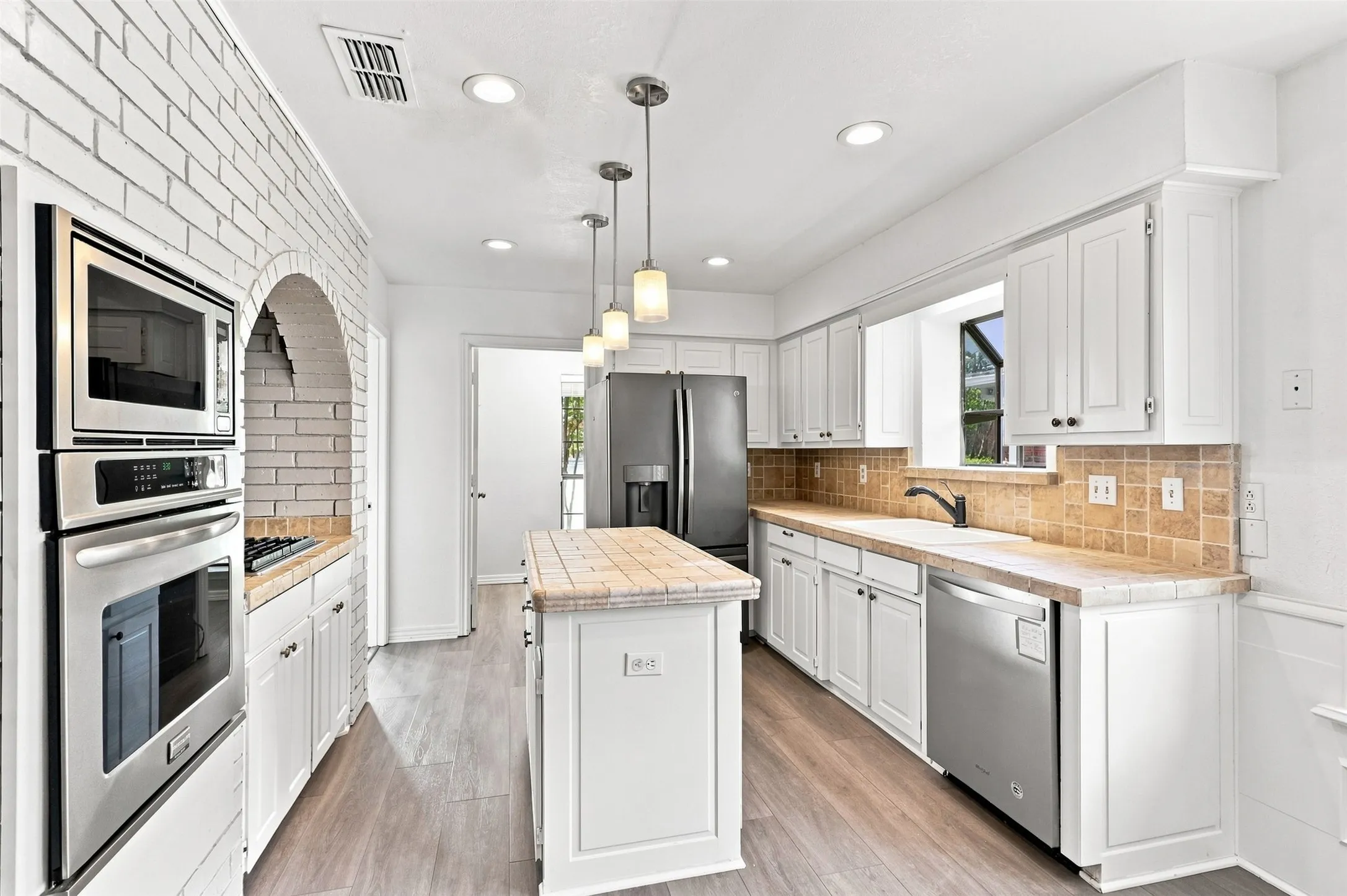White cabinetry with brushed nickel hardware, stainless steel appliances, tile countertops, tile backsplash, and wood-finish flooring