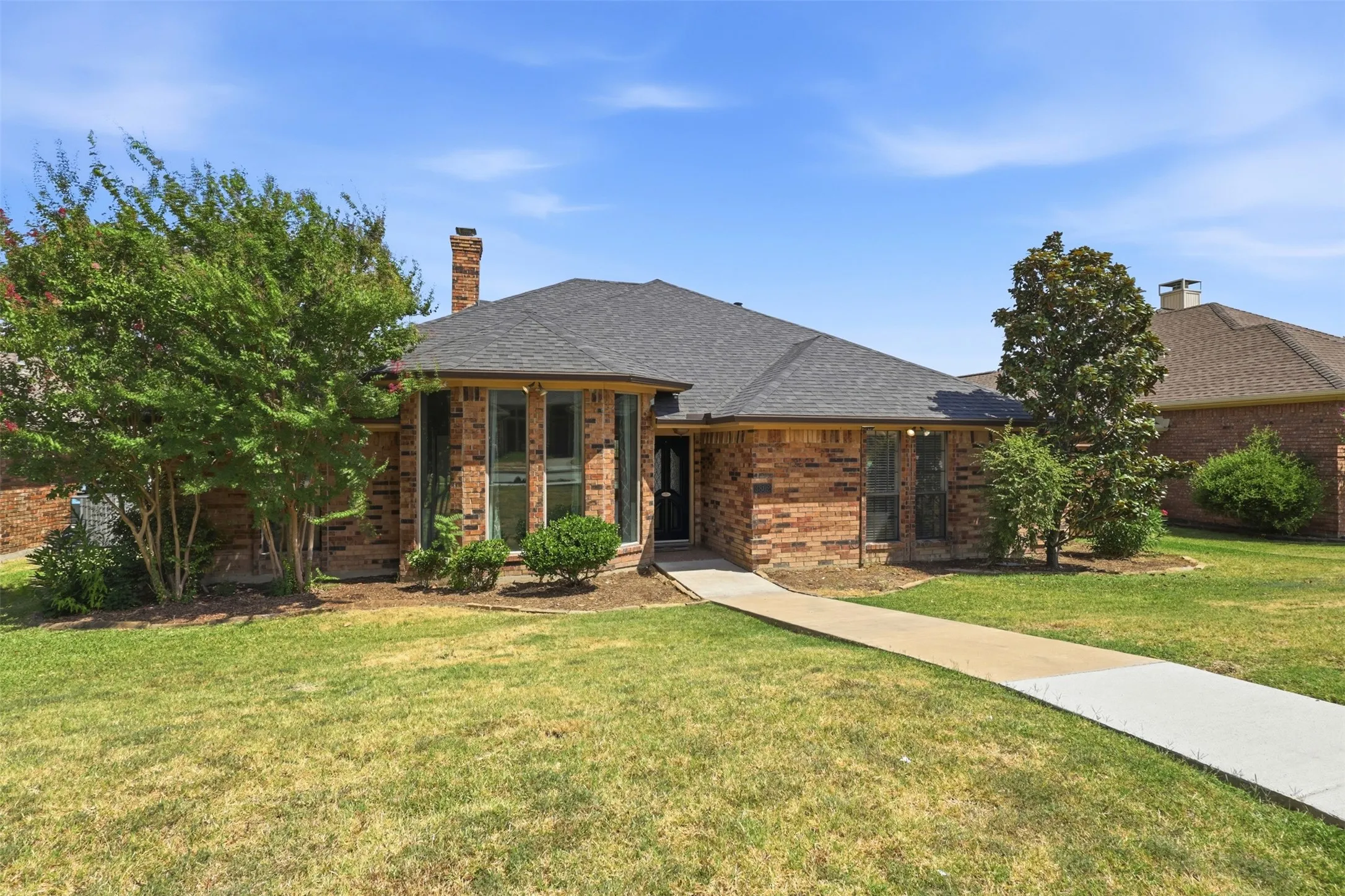 Brick exterior with a dark shingle roof, bay windows, and a paved walkway