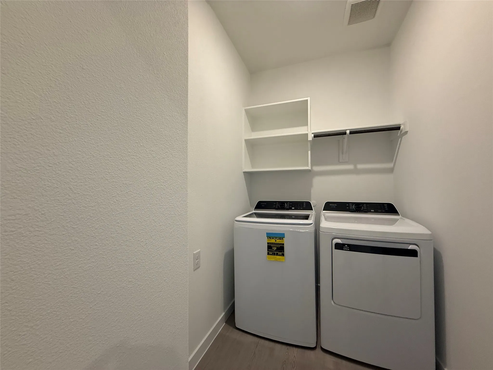 Dedicated laundry space featuring white painted walls, wood-finish flooring, built-in shelving, and a clothing rod