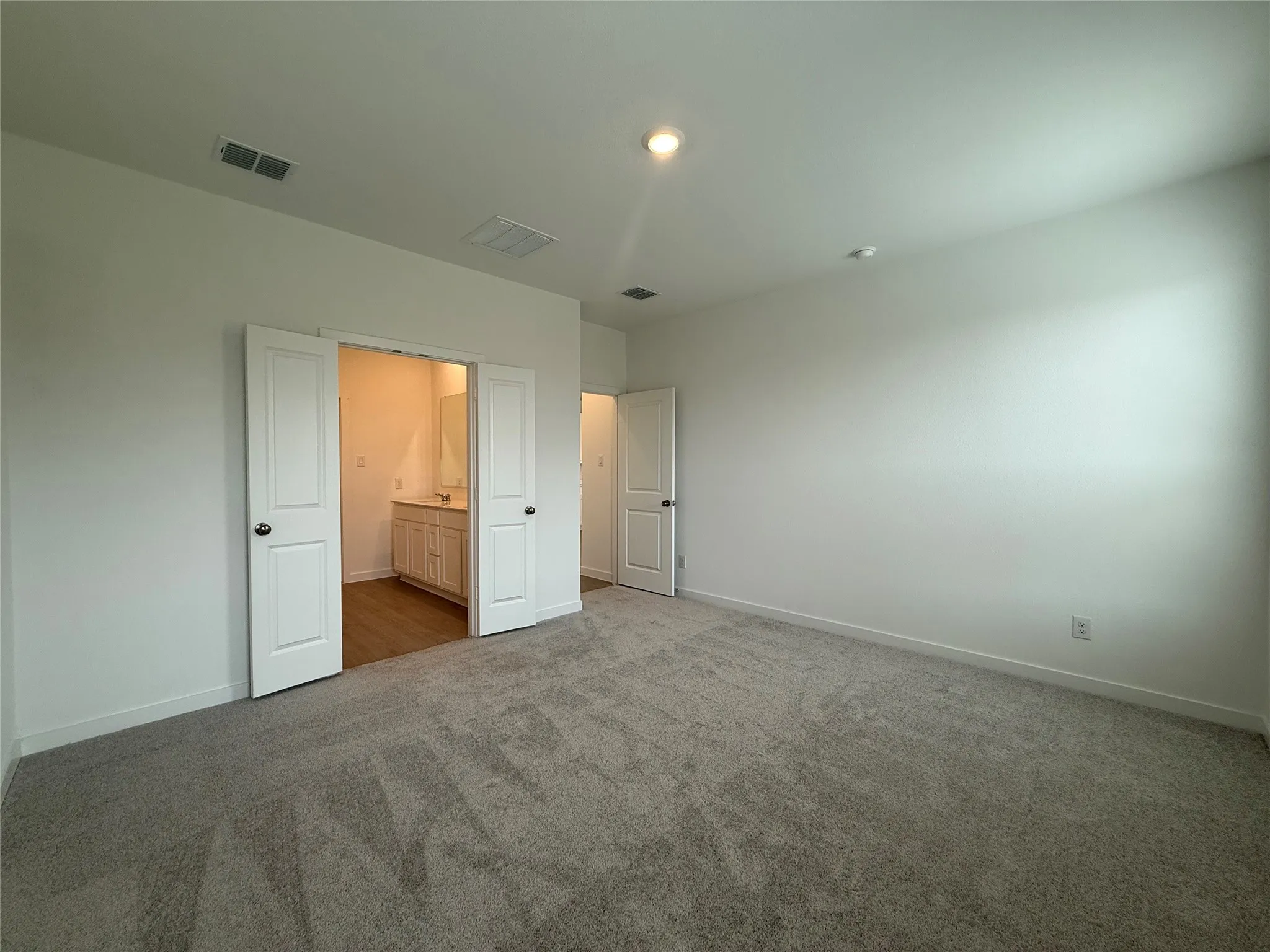 Neutral white walls, recessed ceiling lighting, gray carpet flooring, and an integrated bathroom with a vanity and wood-finish flooring