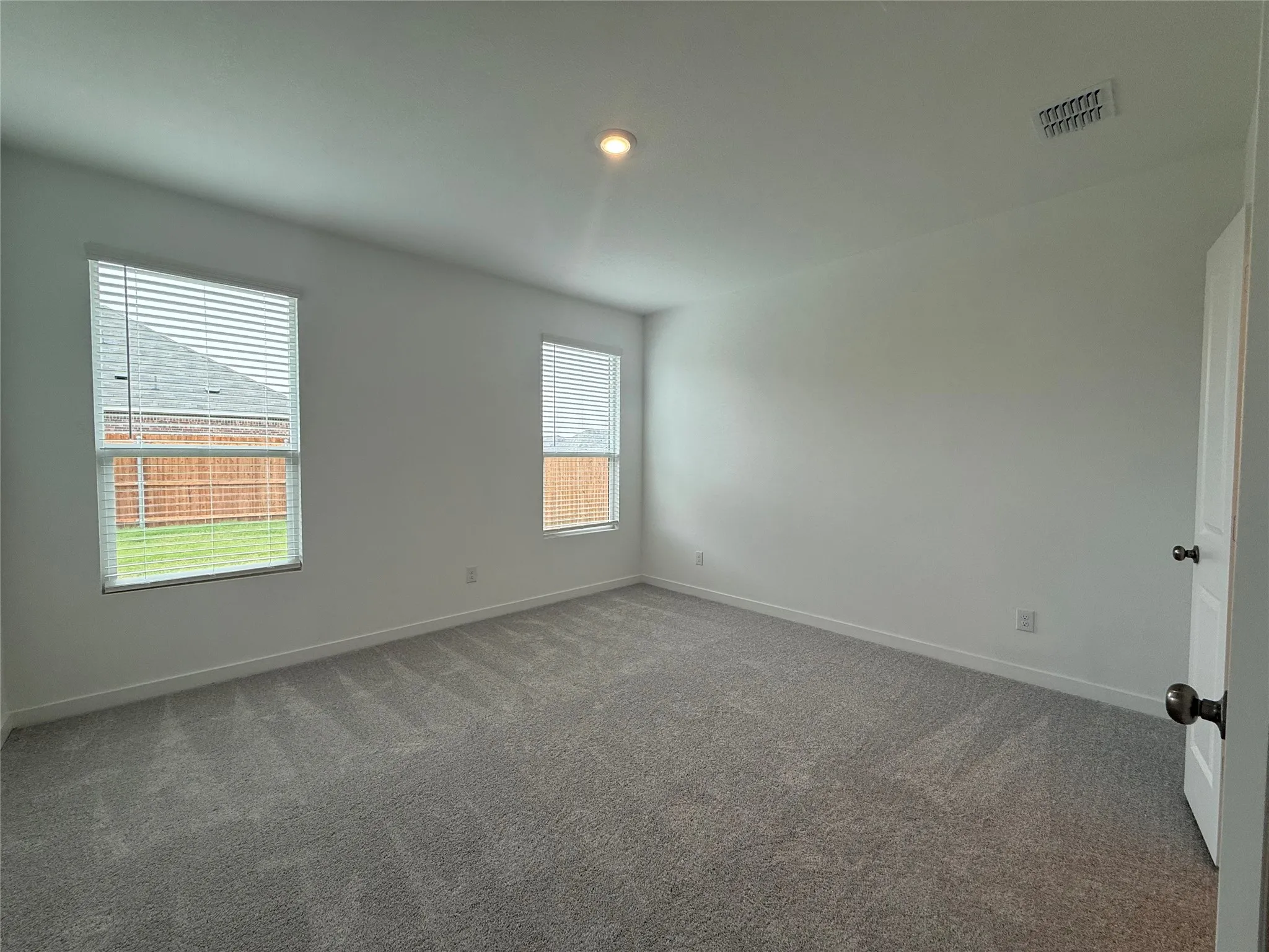 Neutral wall paint, two windows with blinds, recessed ceiling lighting, and gray patterned carpet