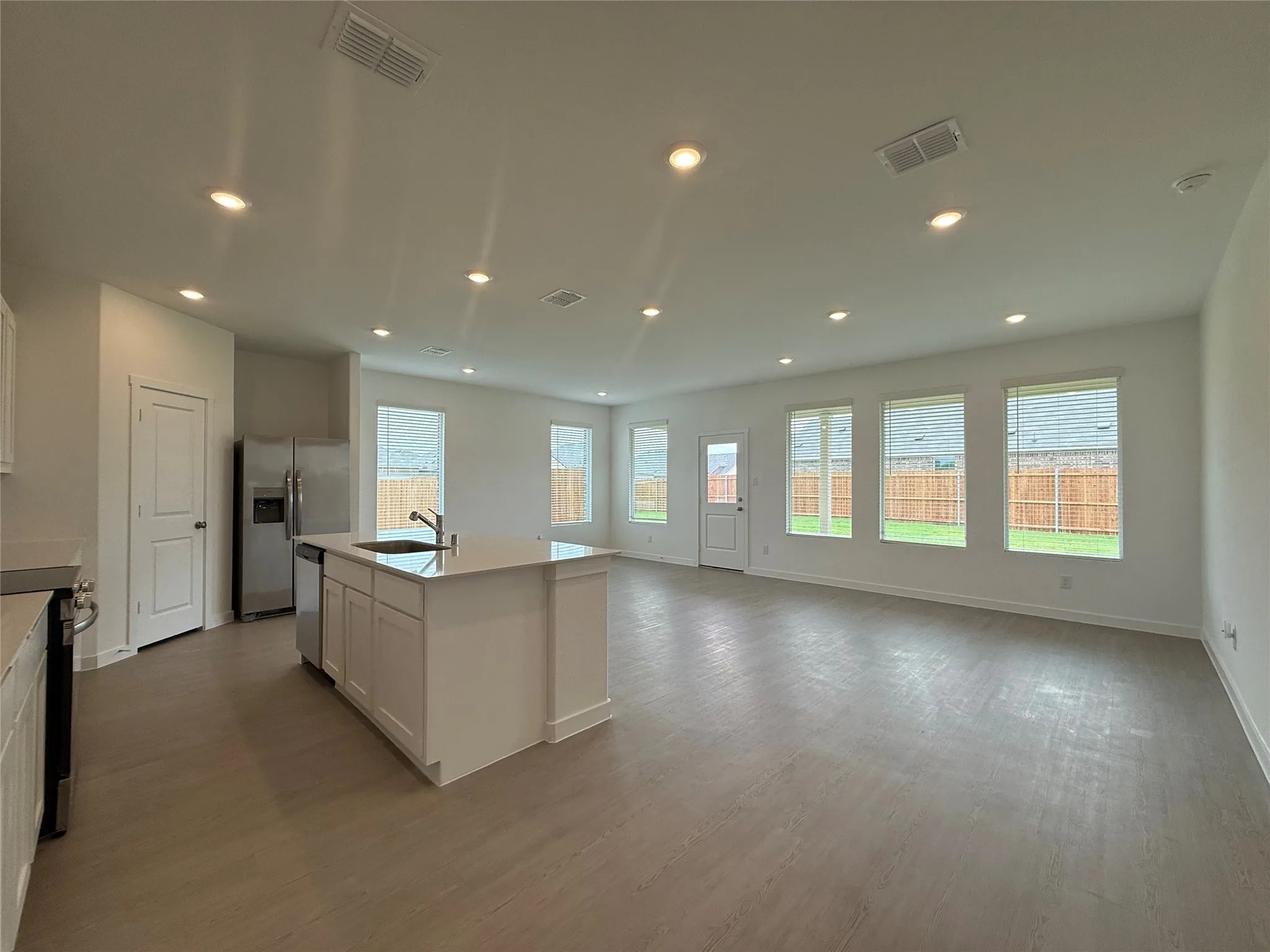 Open-concept living space with recessed lighting, wood-finish flooring, a kitchen island, stainless steel appliances, and multiple windows