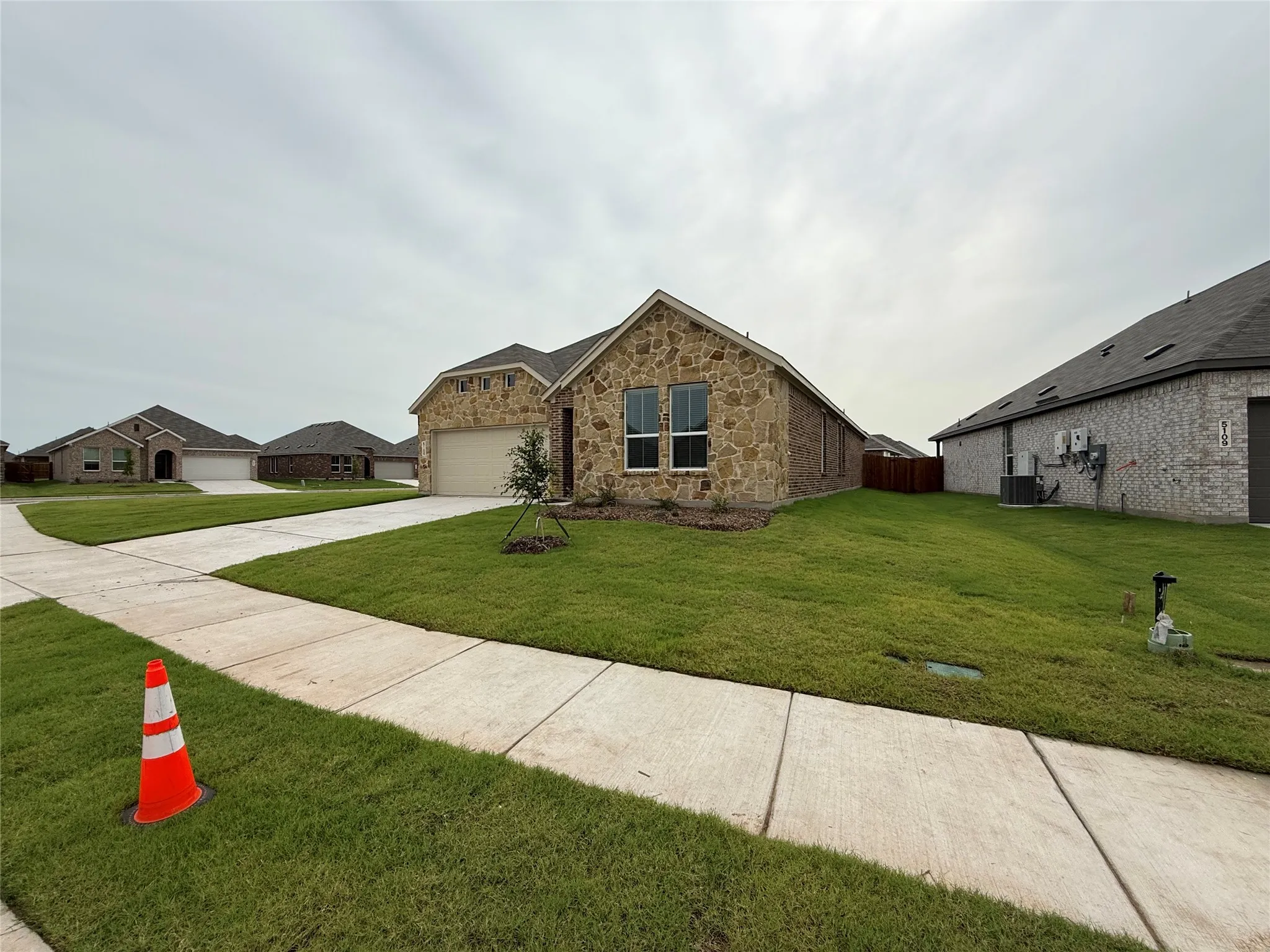 Stone and brick exterior with a two-car garage, concrete driveway, and a front yard with established landscaping