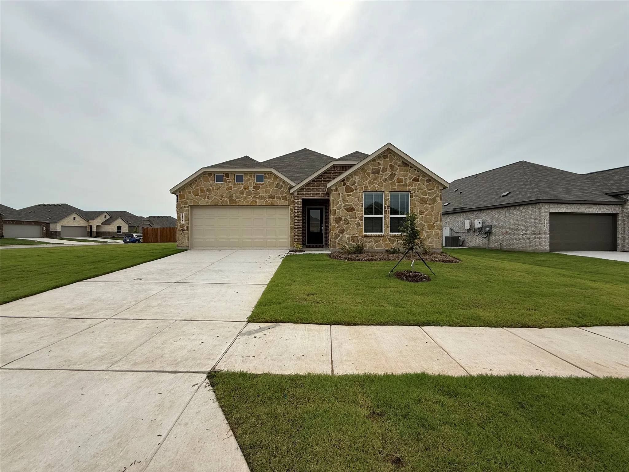Stone and brick facade with a neutral garage door, leading to a concrete driveway and sidewalk