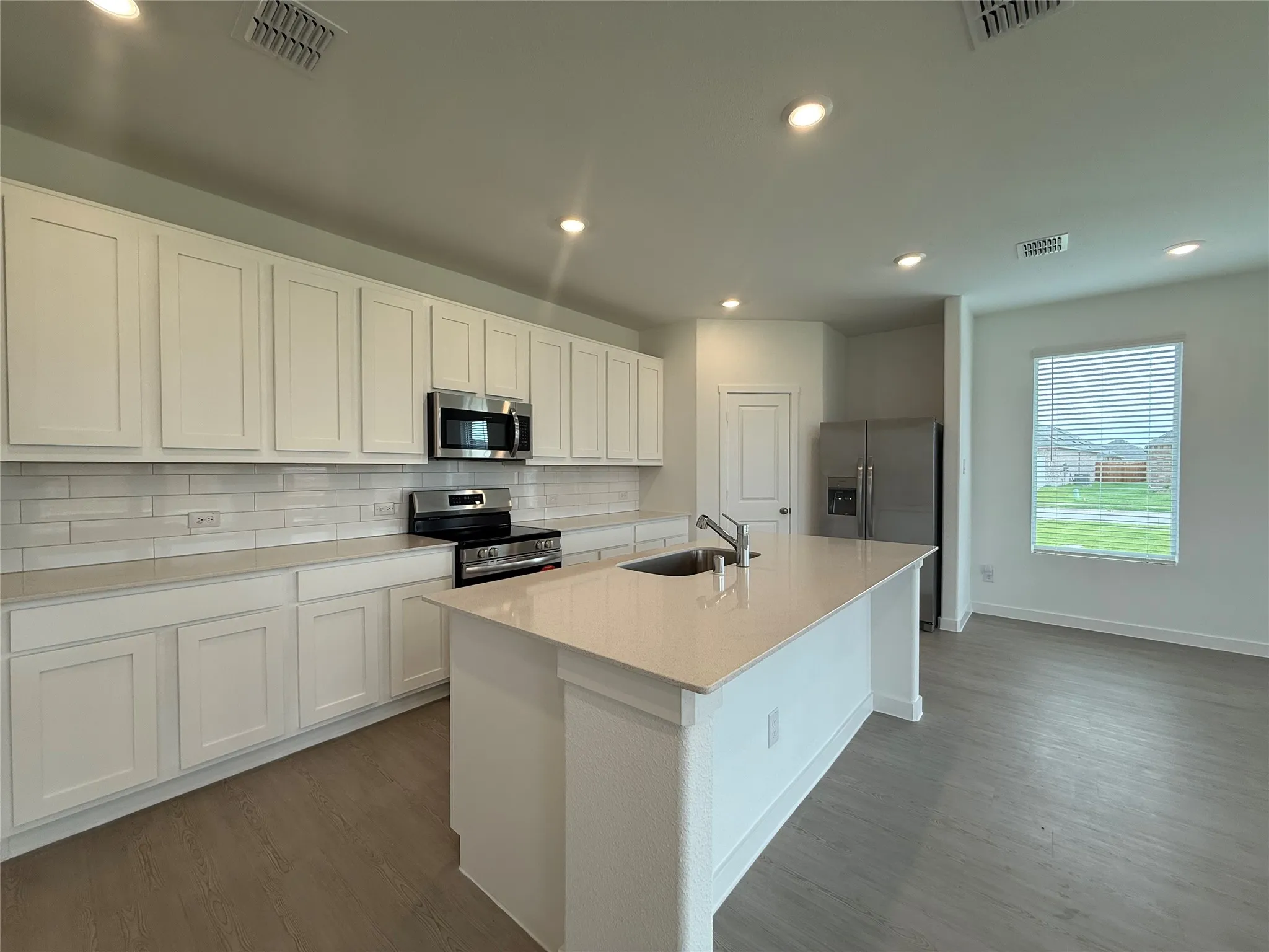 Kitchen featuring white shaker cabinetry, stainless steel appliances, a white subway tile backsplash, a large kitchen island with an undermount sink, and wood-finish flooring