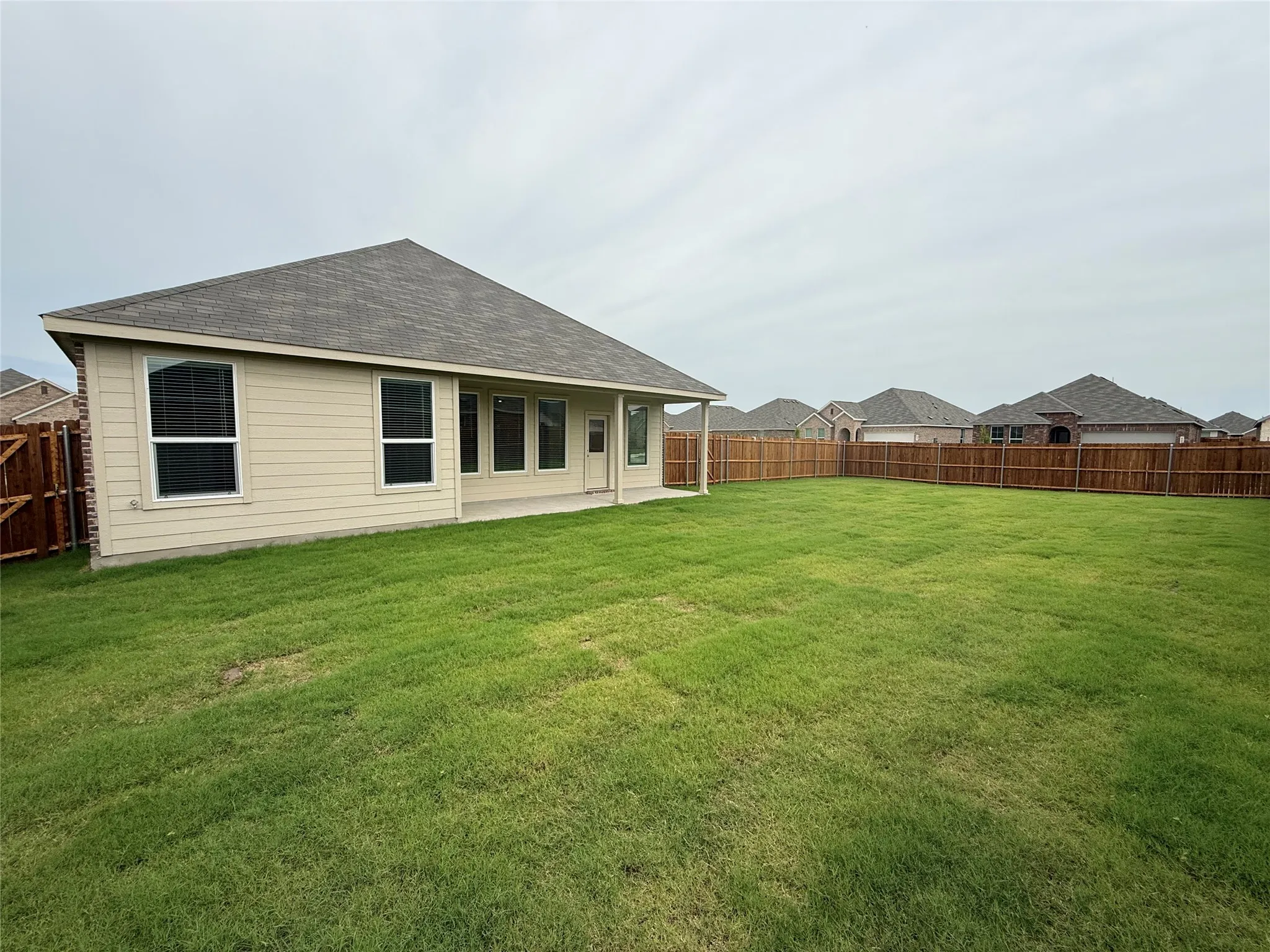 Expansive backyard with a manicured lawn, full wood fencing, and a covered patio area