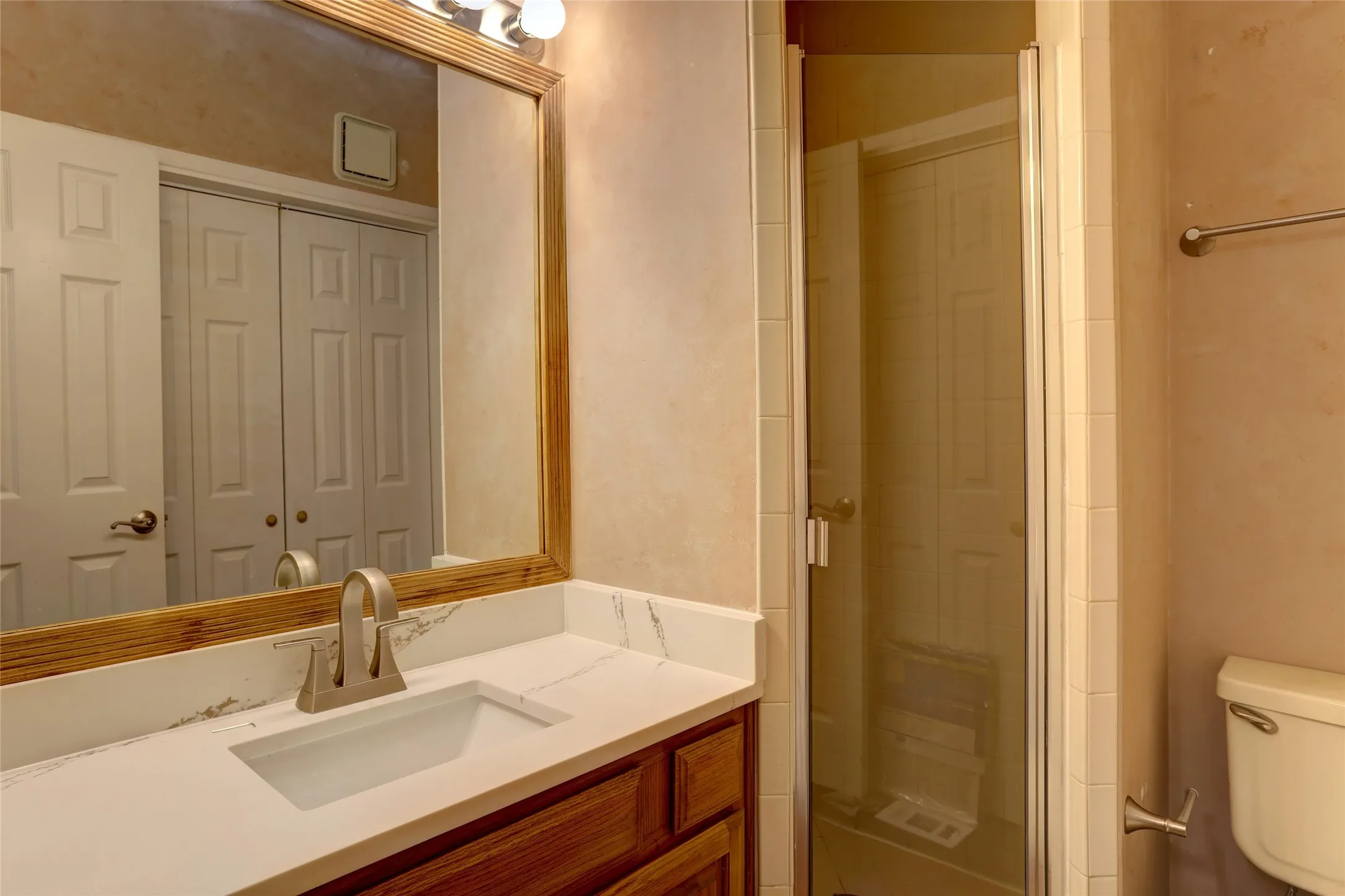 Spa-inspired bathroom featuring a wood-finish vanity, white quartz countertop, and brushed nickel faucet.