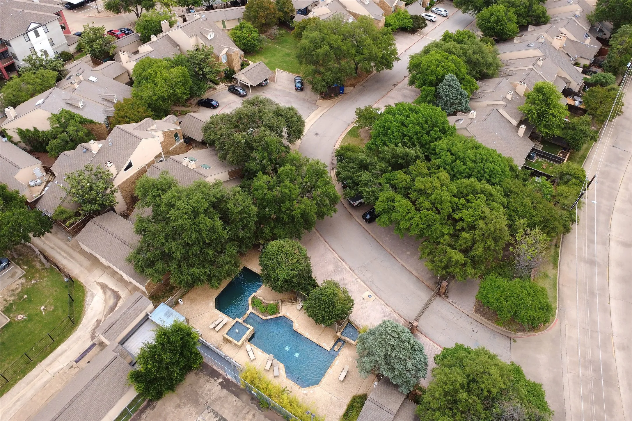 Aerial view of a residential community featuring a resort-style swimming pool with sun loungers and landscaped decking, surrounded by mature trees. A short walk from #120.