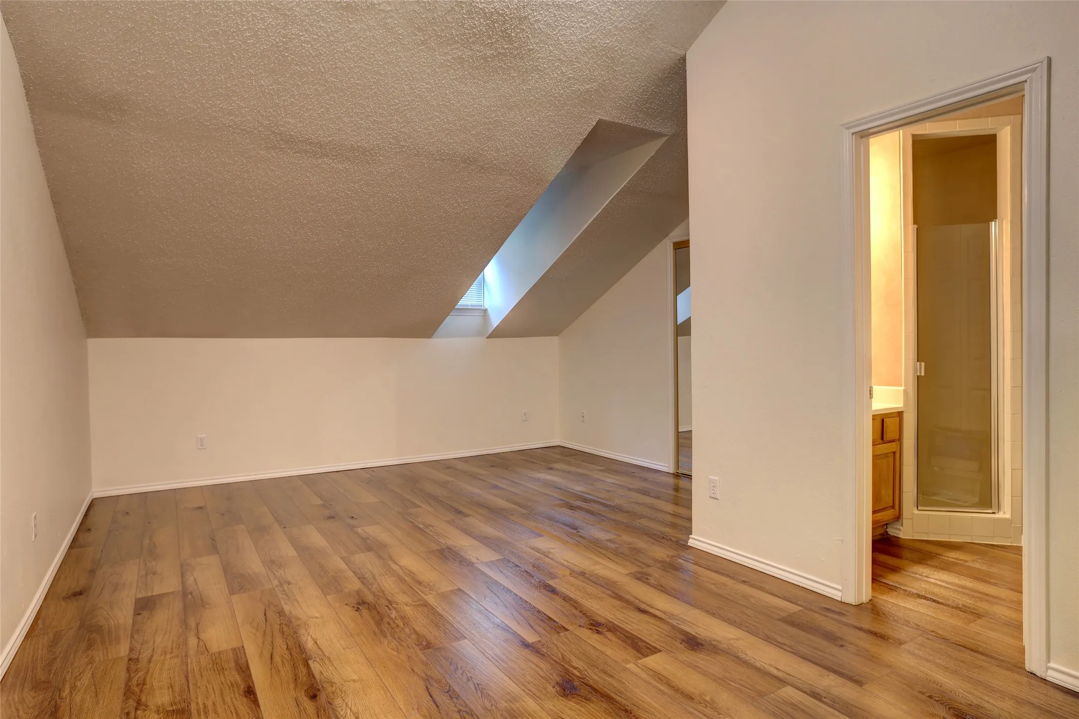 Bright bedroom featuring sloped ceilings with skylight, warm wood-finish flooring, and clean white walls