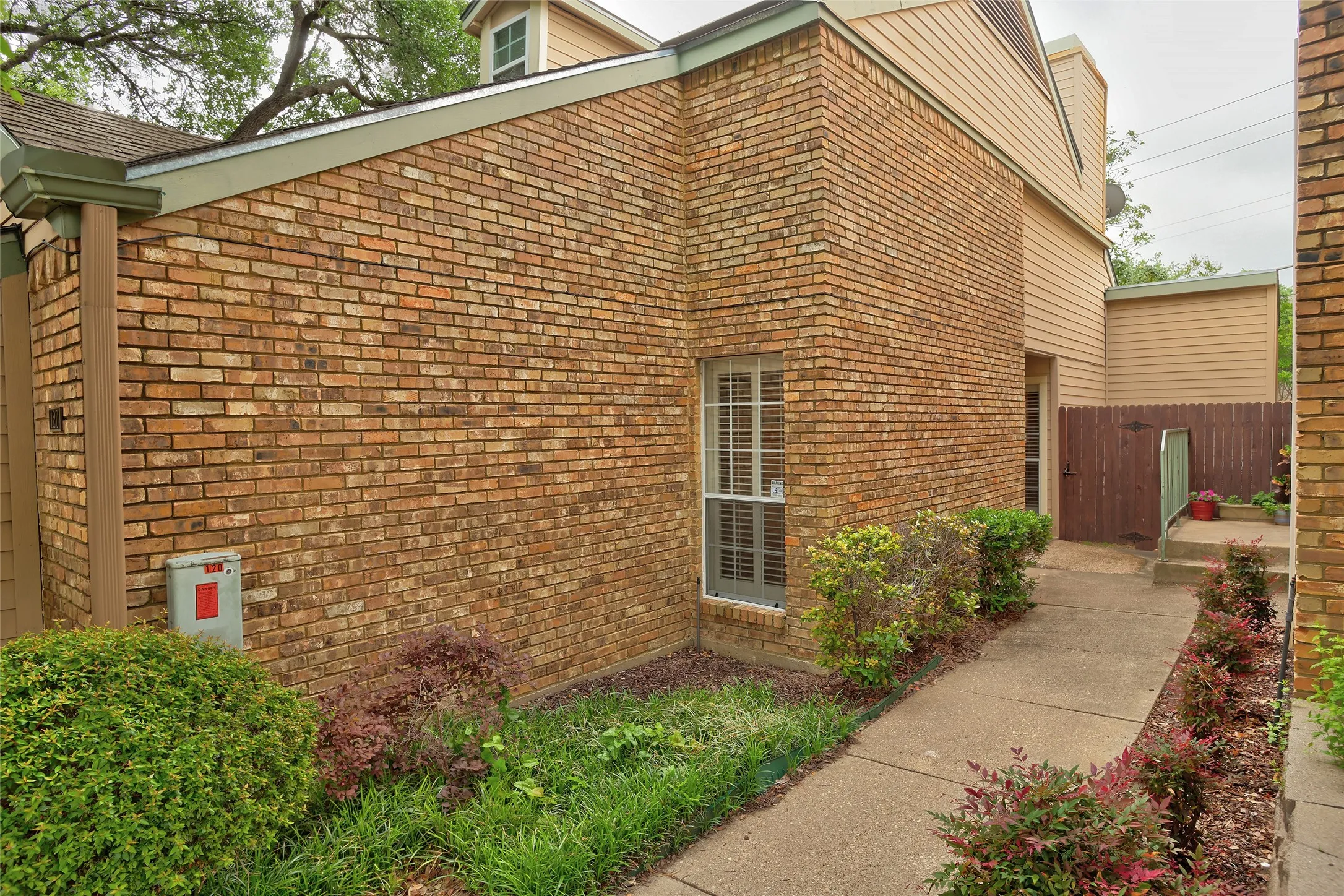 Charming brick exterior with well-appointed landscaping along connecting the carport with the side main entrance.