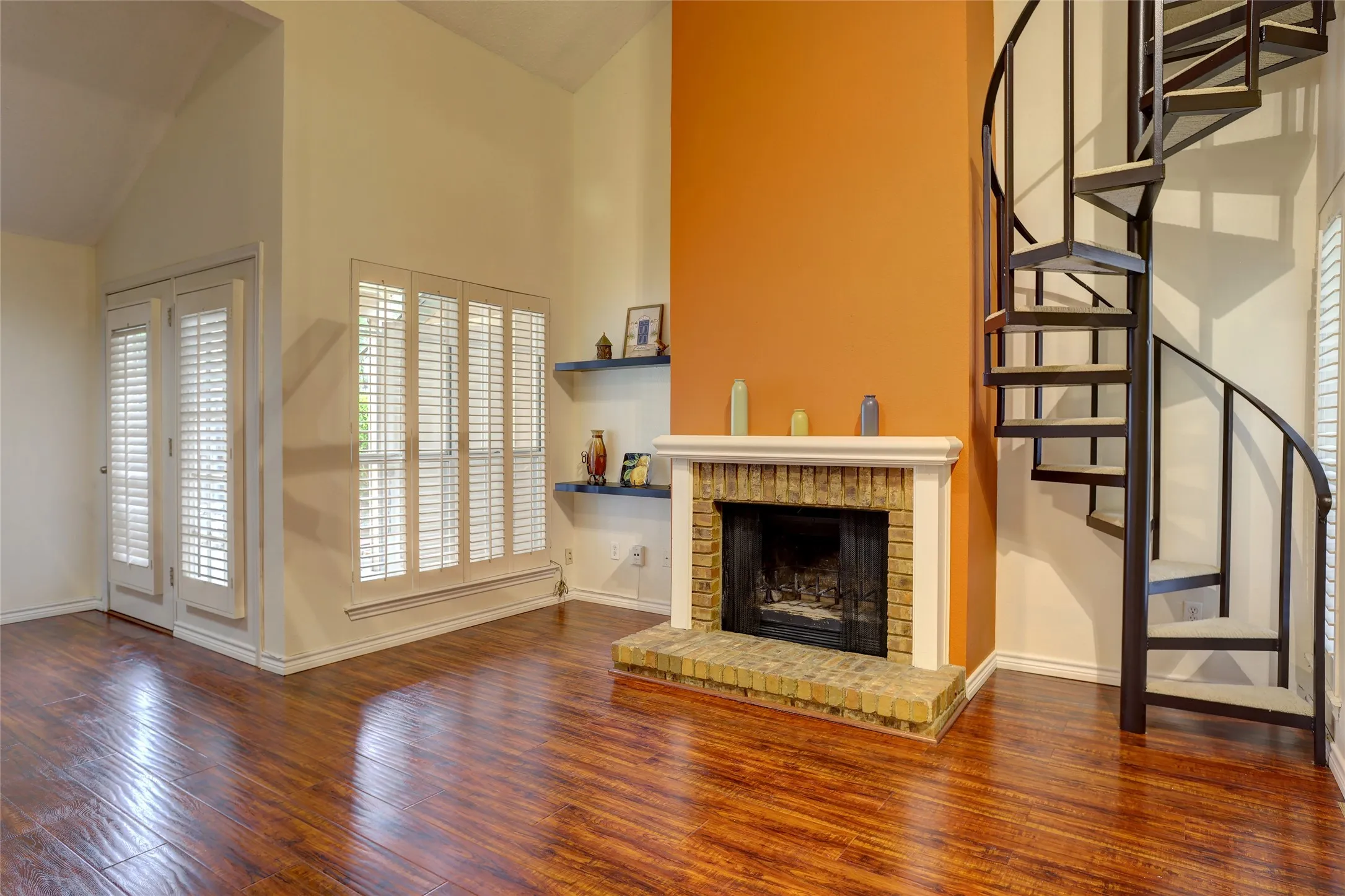 The family's gathering place, high ceiling, wood flooring, brick-surround fireplace, staircase, and plantation shutters.