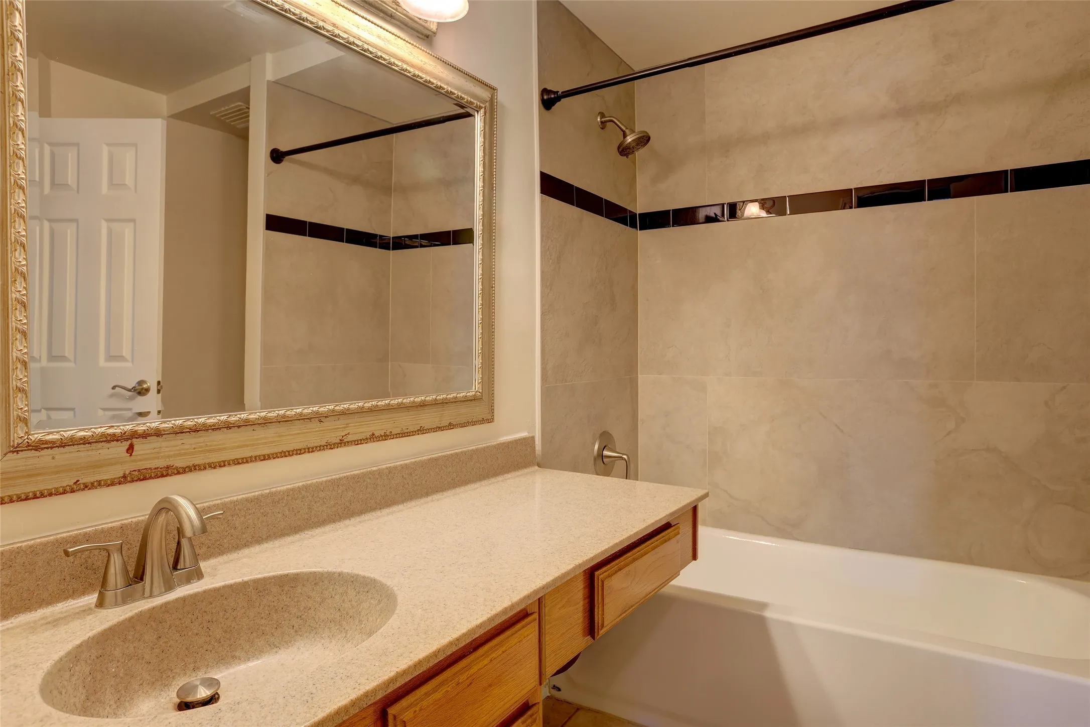 Featuring a wood-finish vanity, cream-colored countertop, and framed mirror with decorative gold trim