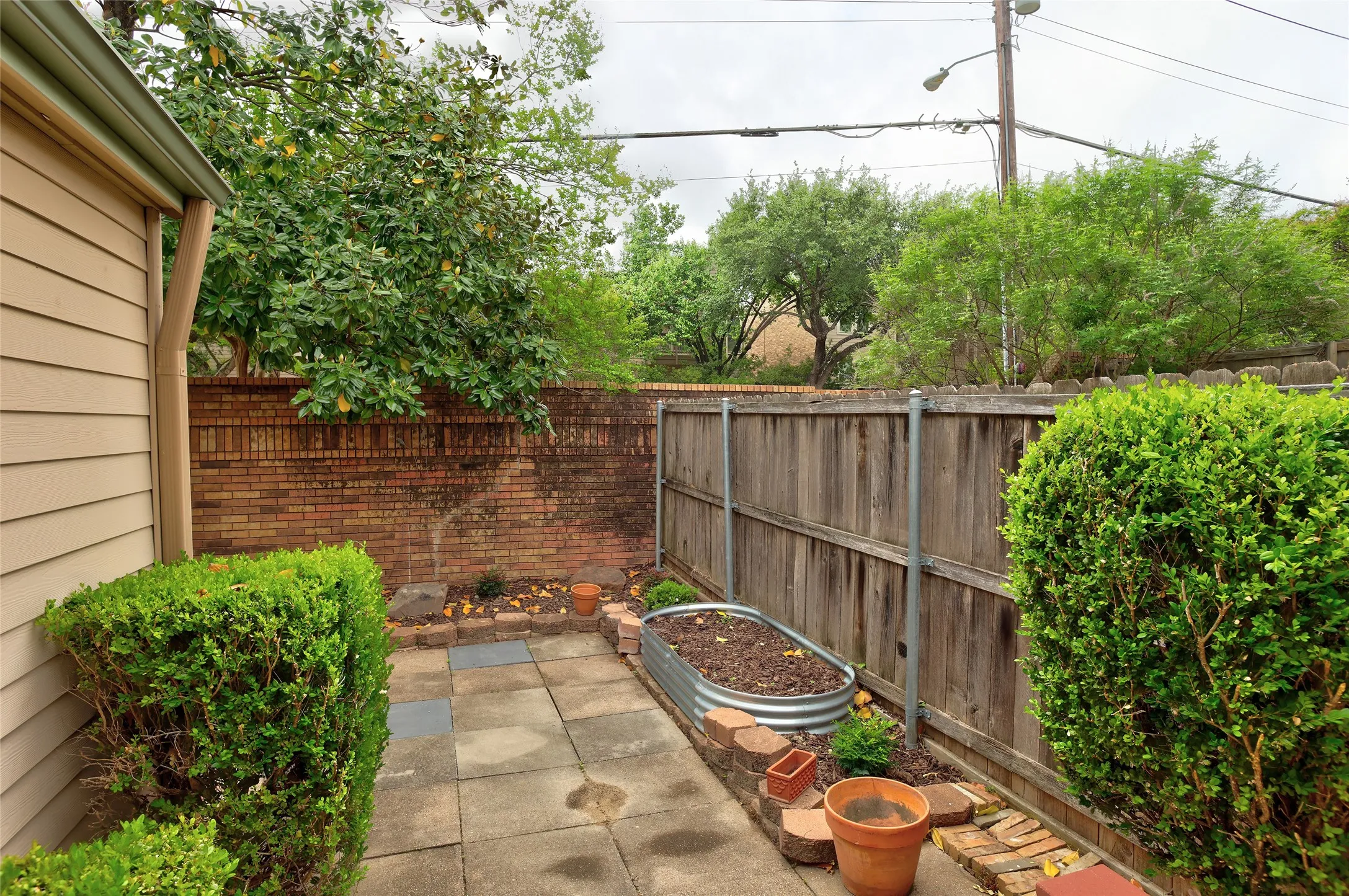 Private backyard retreat featuring mature landscaping with manicured hedges, brick hardscaping, wood-finish fencing, and established shade trees