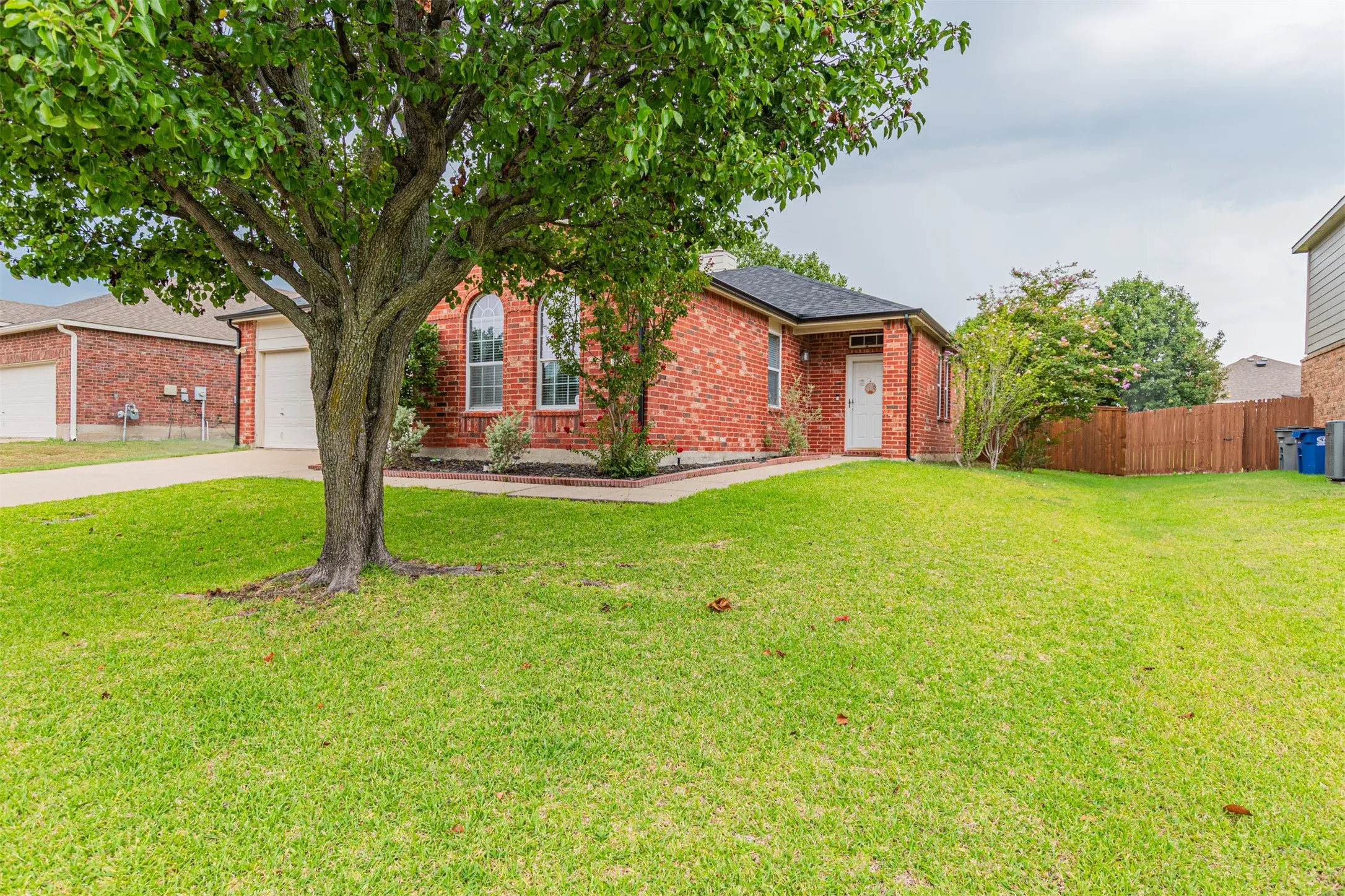 Red brick exterior with arched windows, an attached garage, a white entry door, and a wood privacy fence