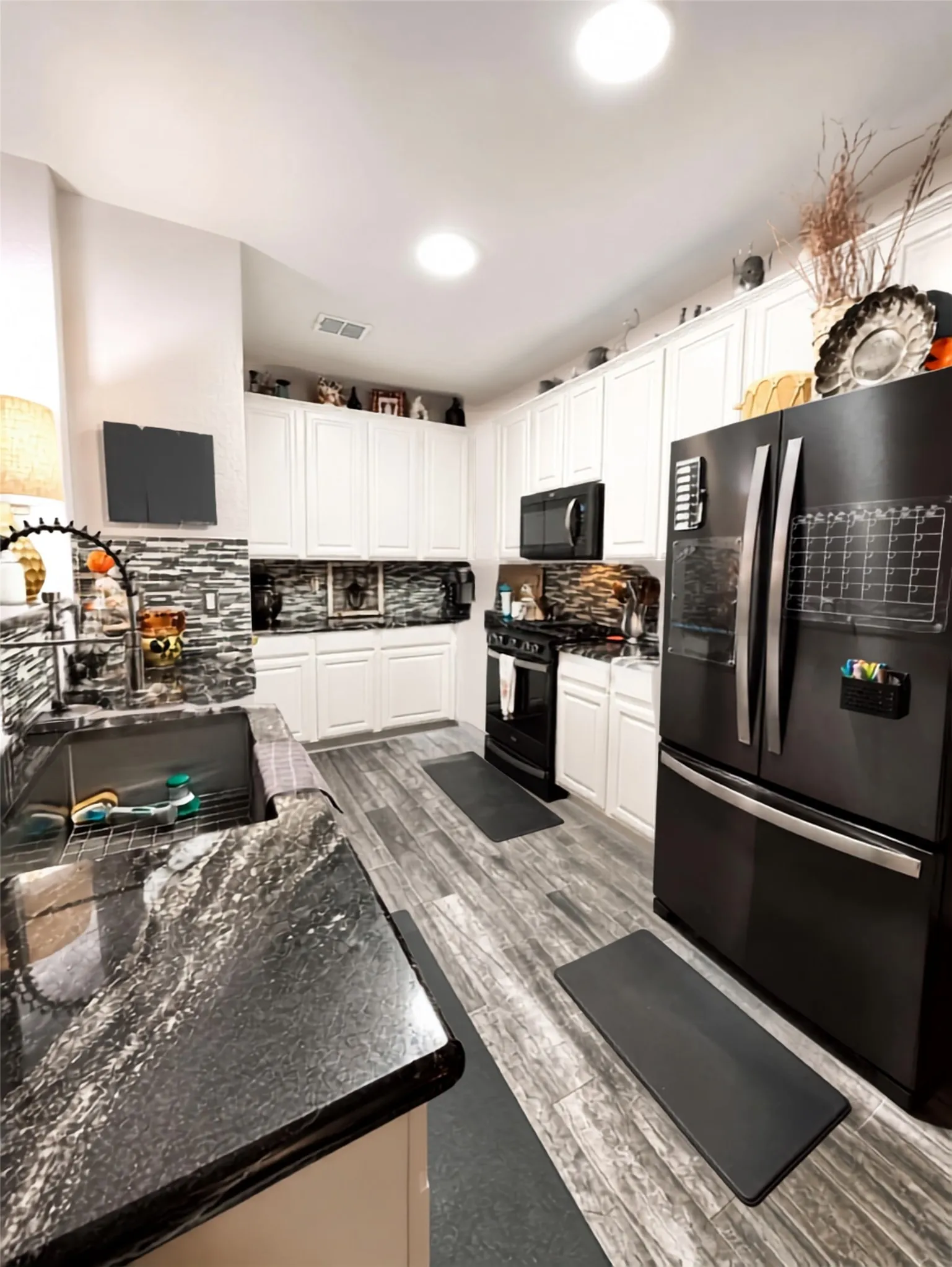 White cabinetry with black hardware, black and gray backsplash, black appliances, wood-finish flooring, and black granite countertops