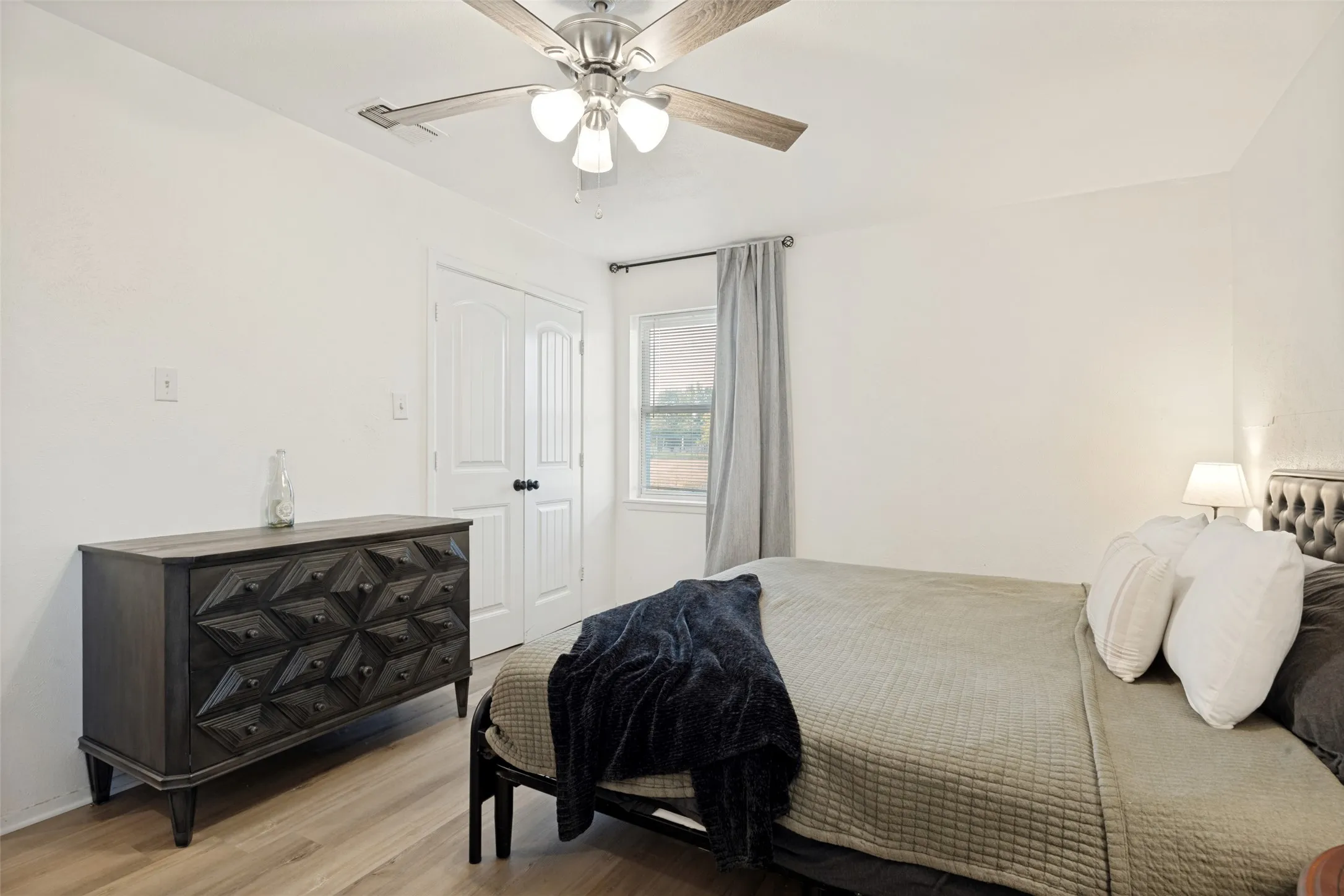 Bright interior featuring wood-finish flooring, a ceiling fan with integrated lighting, and a window with curtain rod
