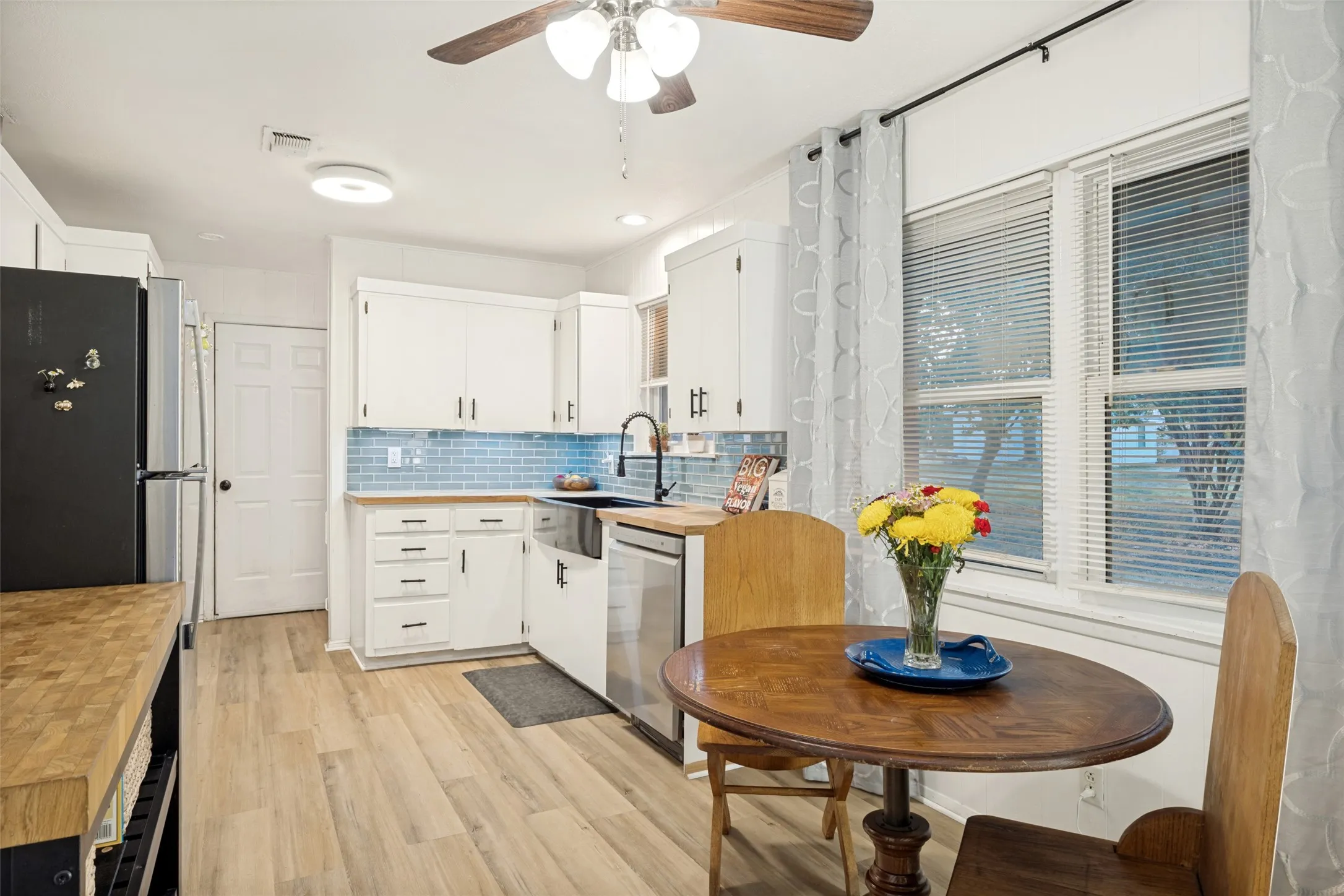 Kitchen featuring light wood-finish flooring, white cabinetry, a blue subway tile backsplash, and a double window