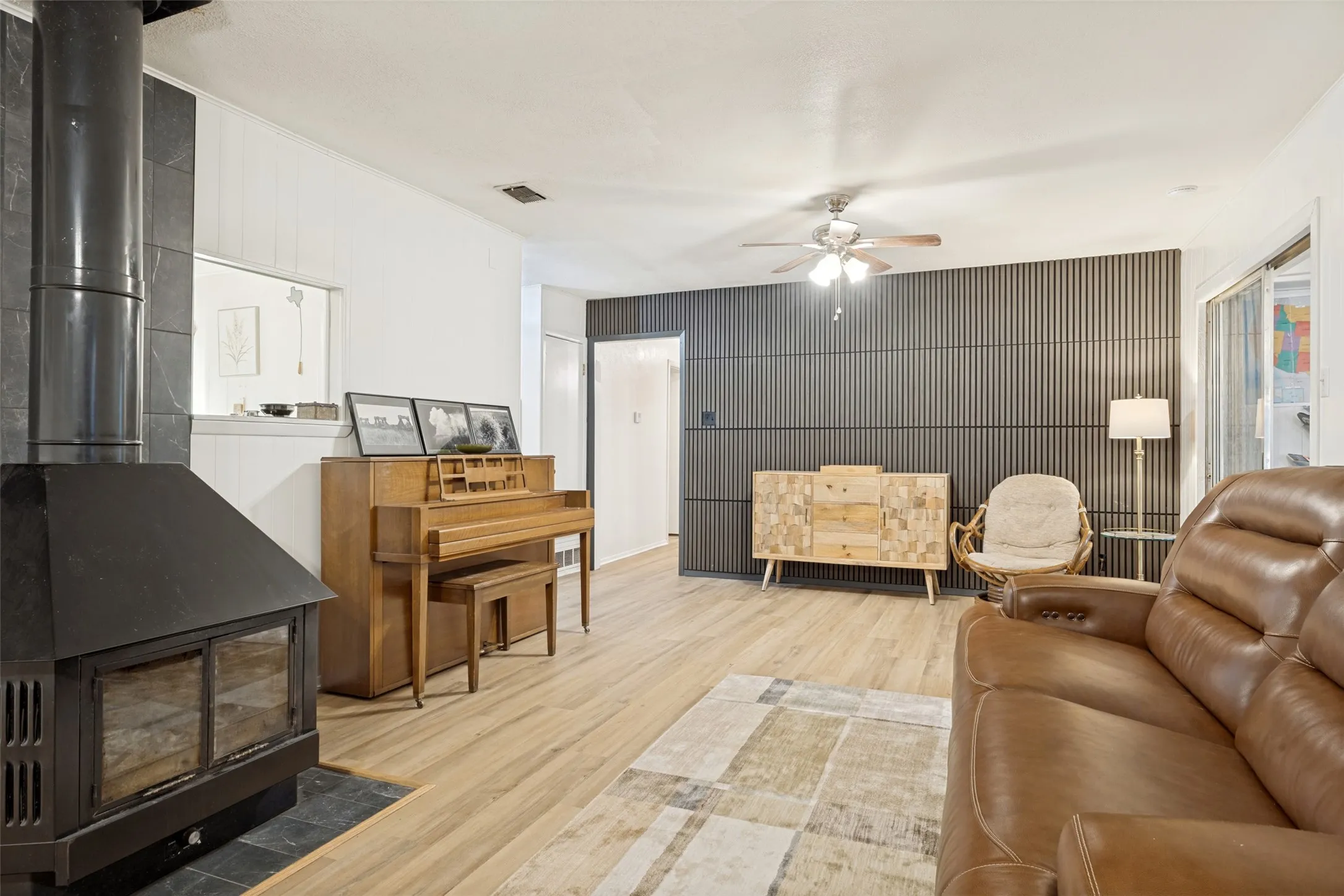 Wood-finish flooring throughout, a black metal fireplace with a slate hearth, and a contemporary accent wall with vertical paneling
