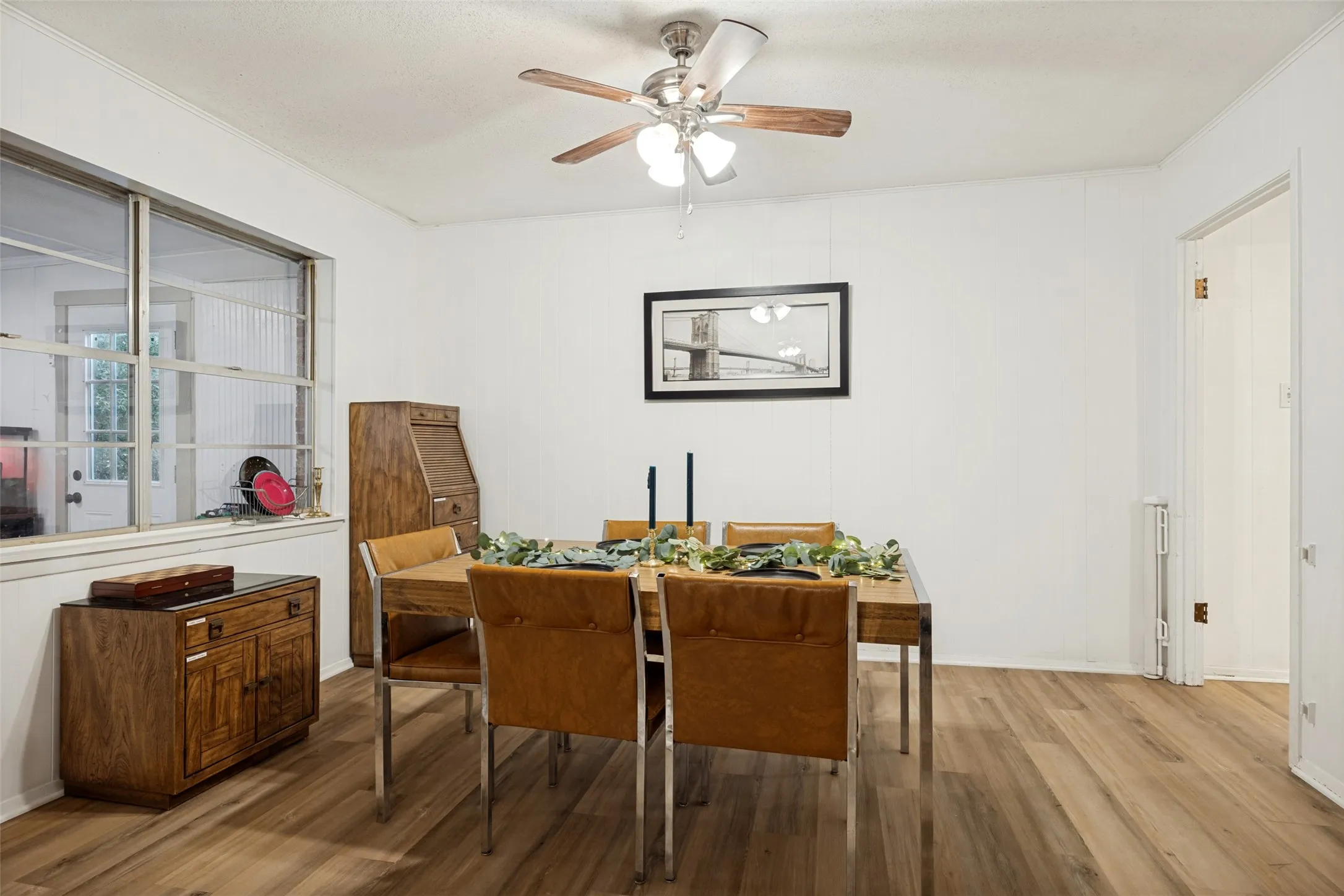 Wood-finish flooring with a ceiling fan light fixture and large windows