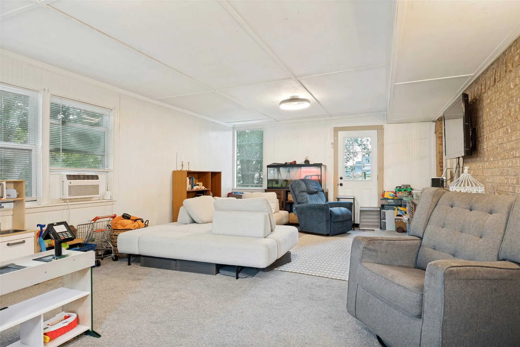 Carpeted room with a brick accent wall, multiple windows, and a white paneled door