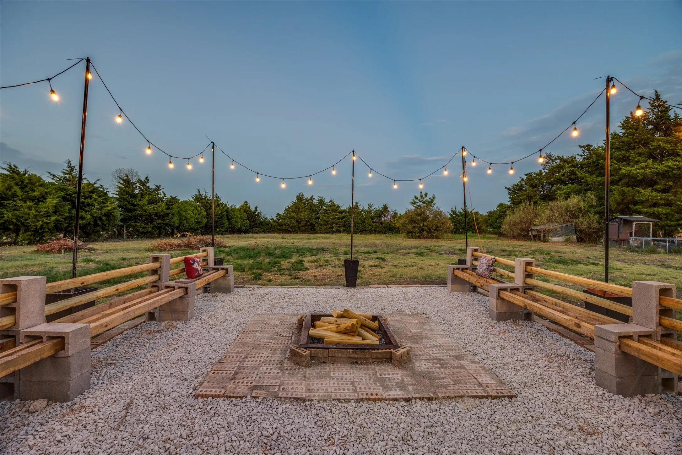 Gravel patio featuring a built-in fire pit, string lights, and bench seating constructed with wood and concrete blocks