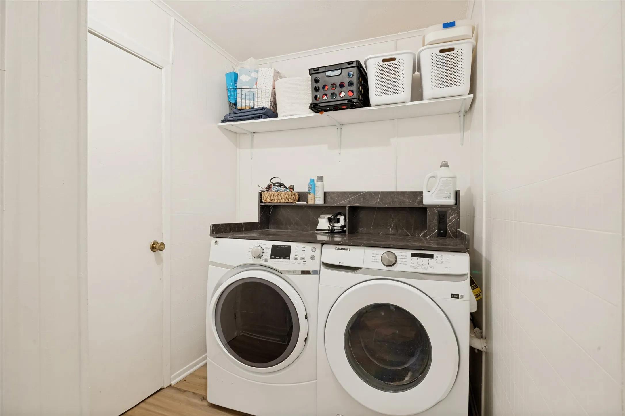 Laundry area with wood-finish flooring, white walls, and a built-in shelf