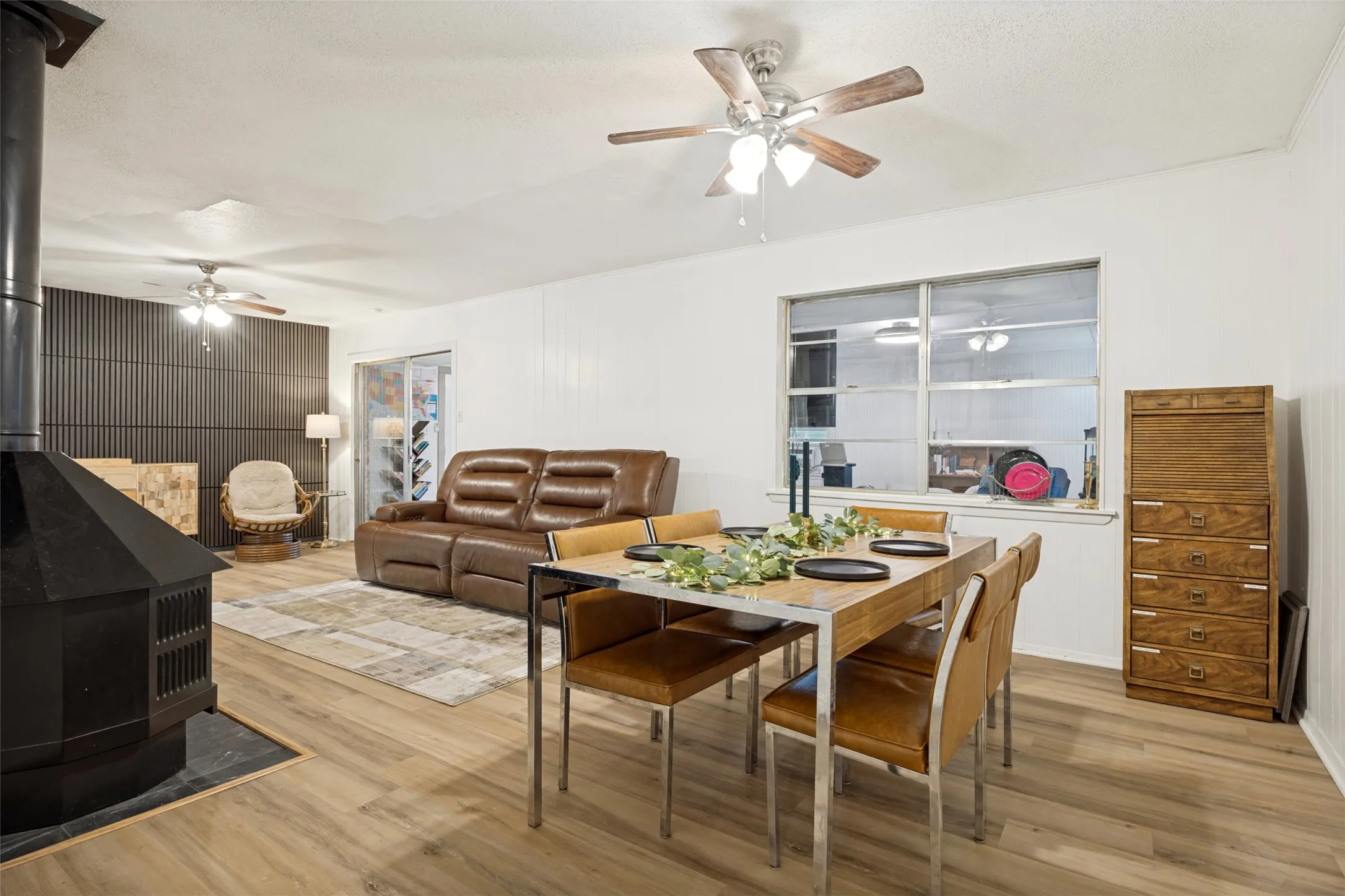 Open concept living and dining area featuring wood-finish flooring, a built-in fireplace with a black slate hearth, and a contemporary accent wall