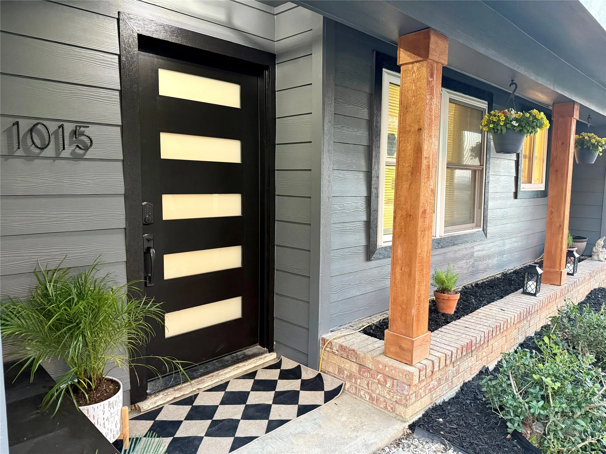 Modern front door with opaque glass inserts, grey horizontal siding, and natural wood columns