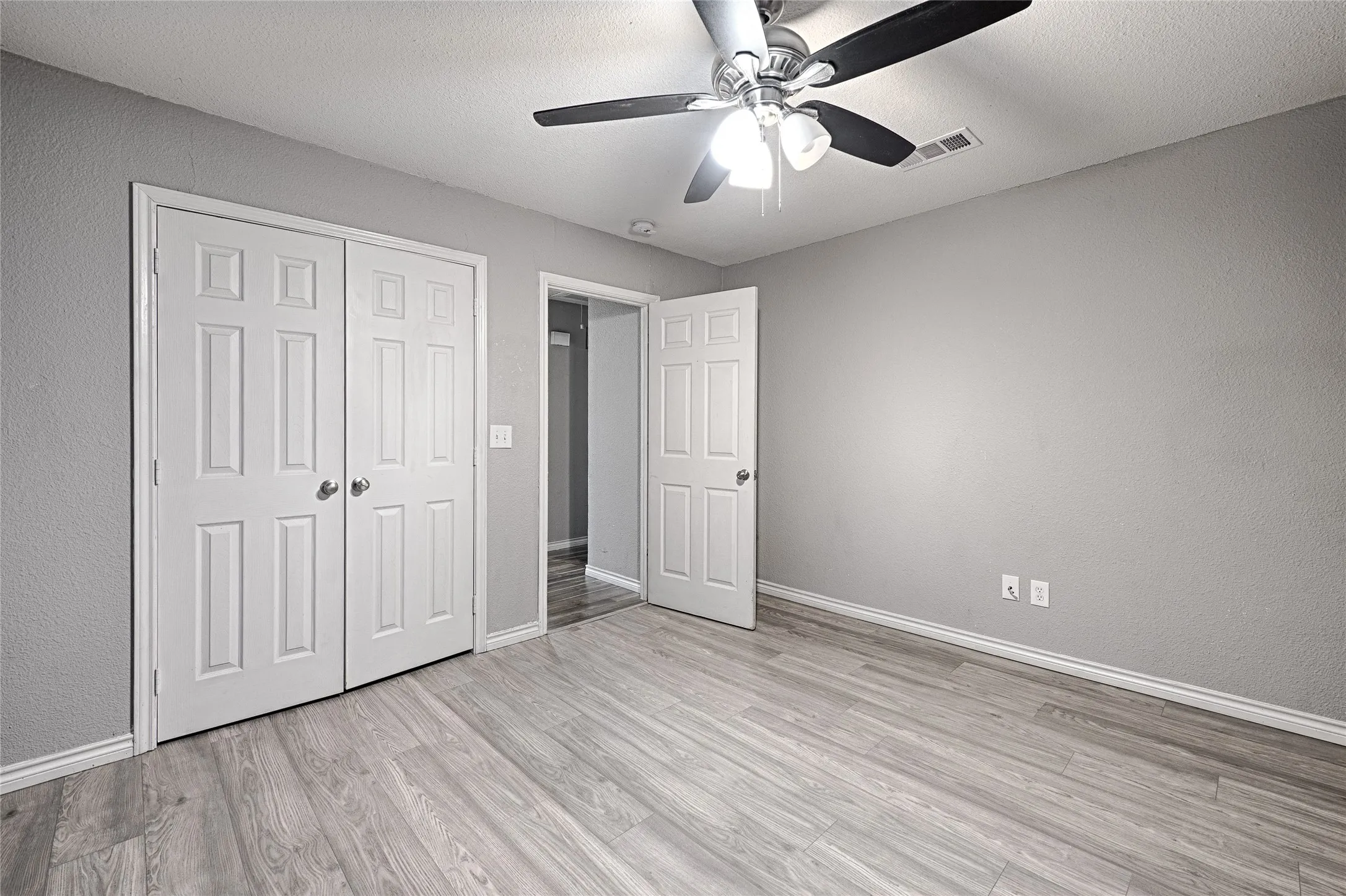 Wood-finish flooring, ceiling fan with light fixture, neutral wall color, white trim, and bi-fold closet doors