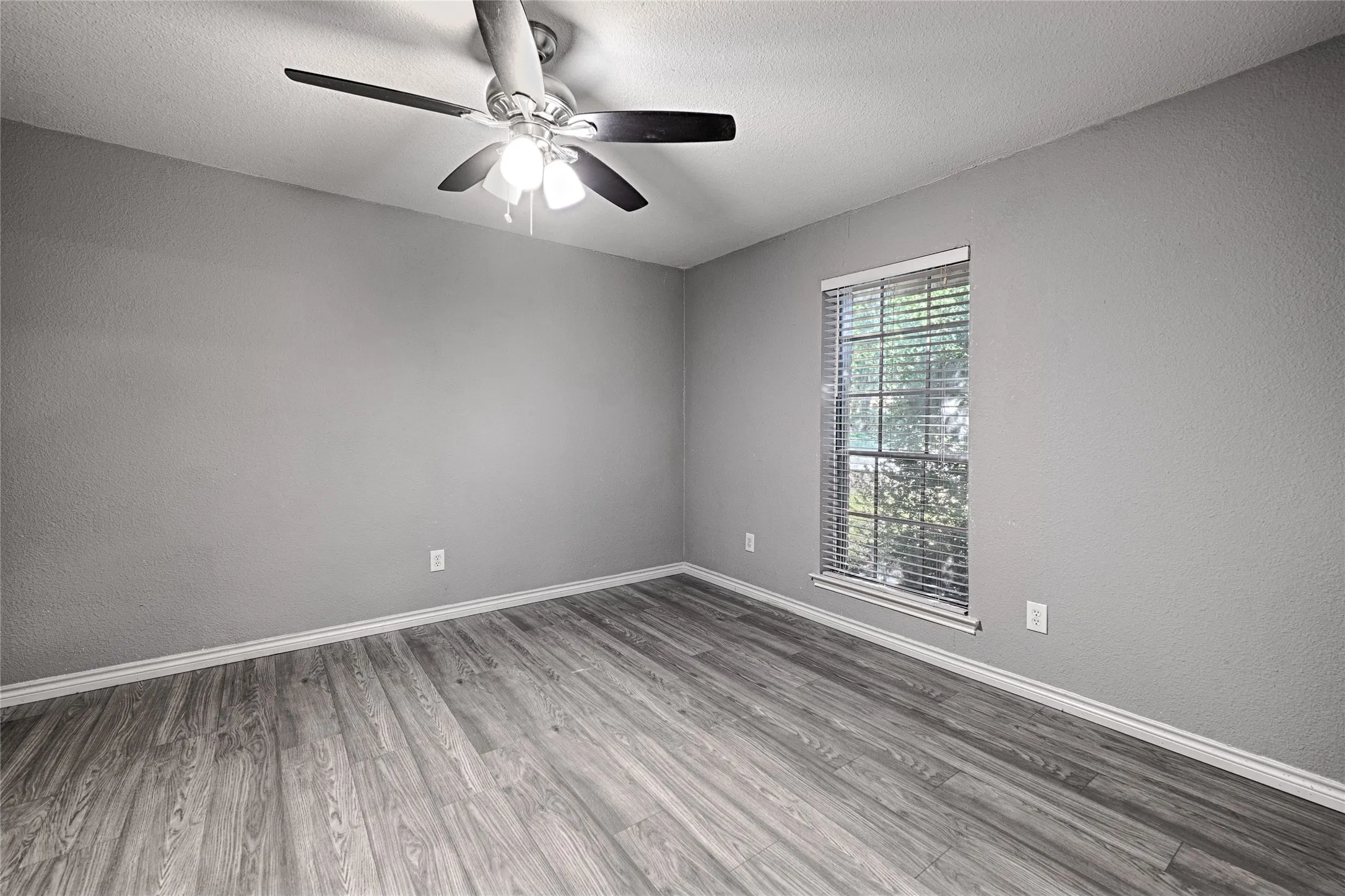 Wood-finish flooring, single window with blinds, ceiling fan with integrated lighting, and neutral wall tones