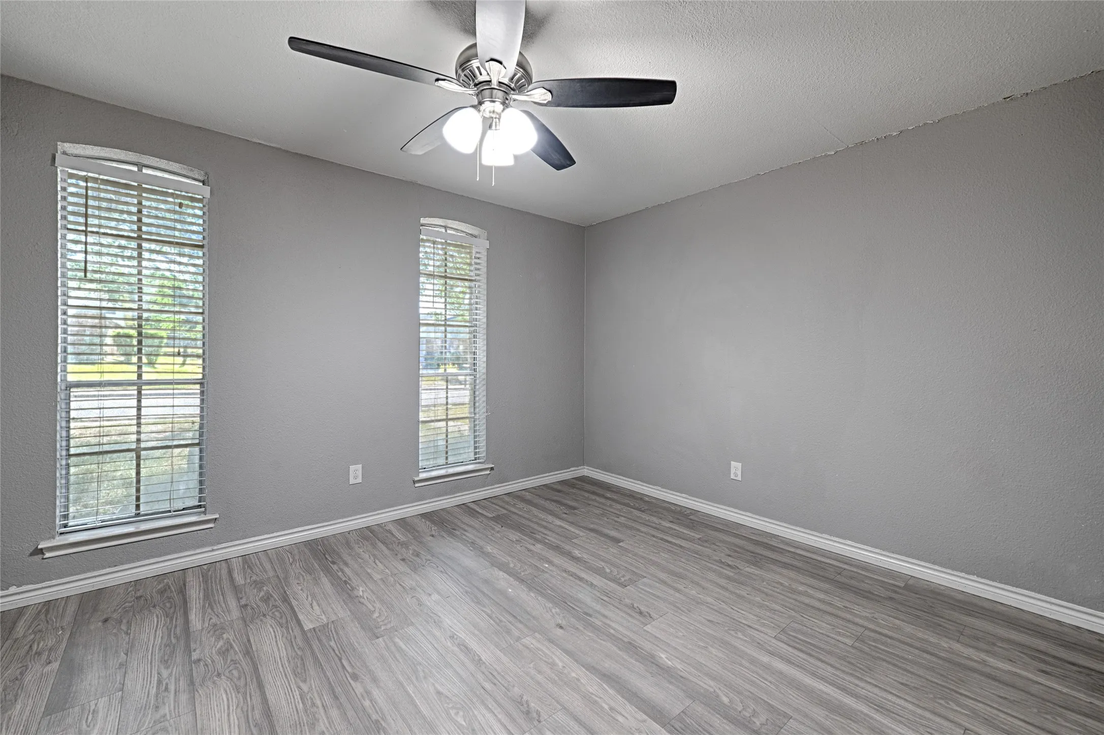 Wood-finish flooring, two windows with blinds, ceiling fan with integrated lighting